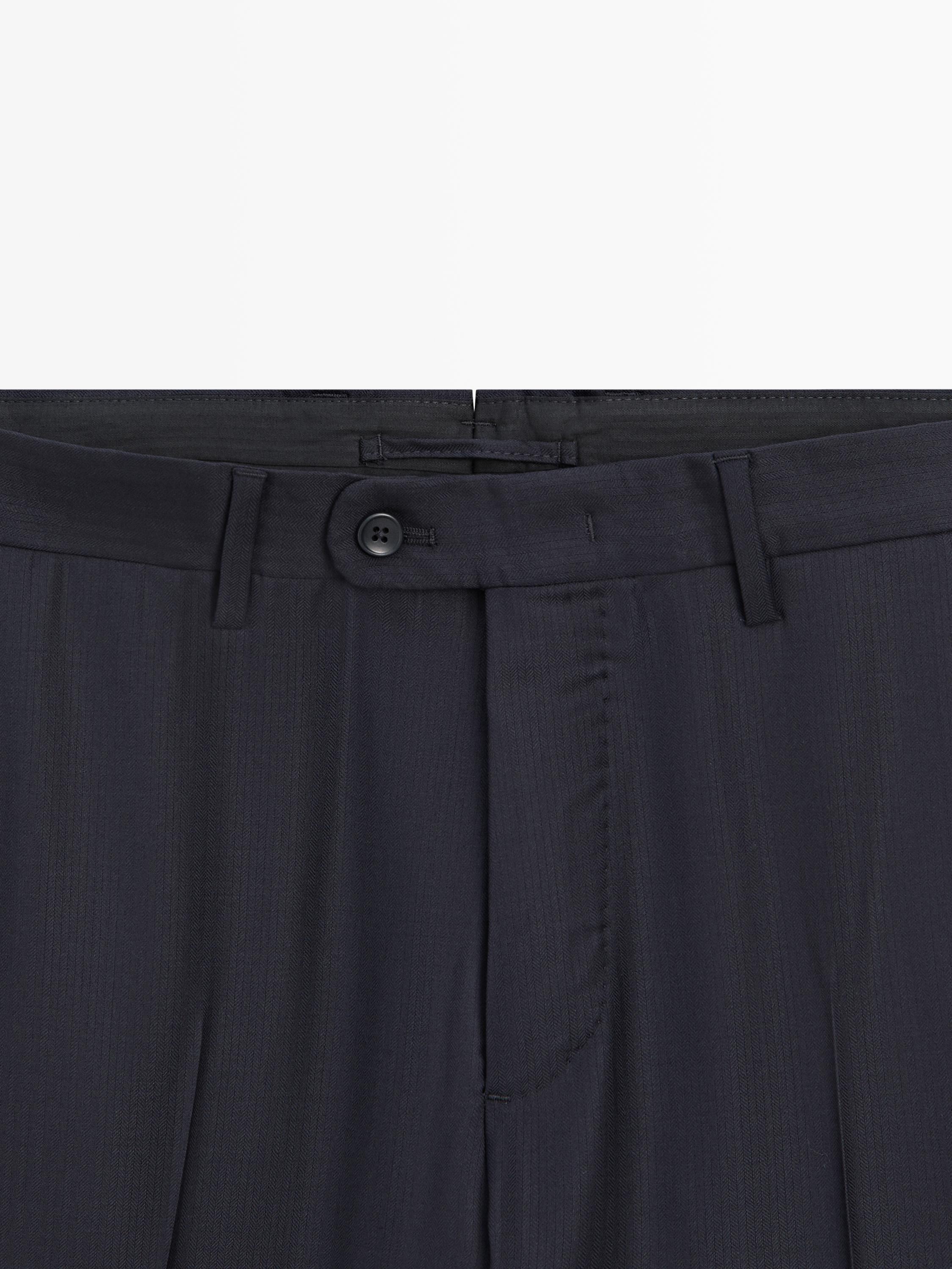 Λεπτομέρεια μέσης παντελονιού κοστουμιού σε ναυτικό μπλε με μπροστινό κουμπί και θηλιές ζώνης.