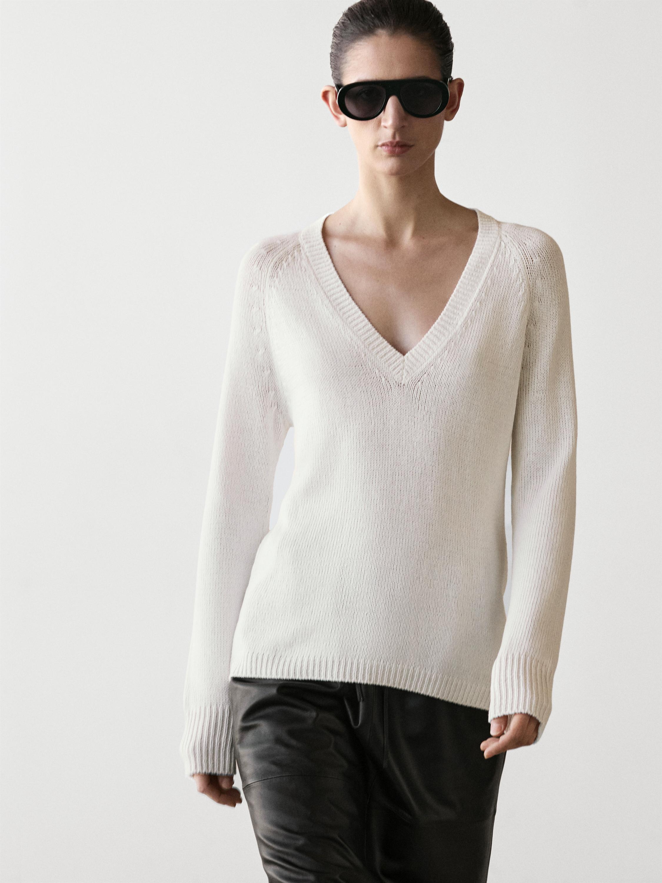 Ensemble pull blanc en maille col en V et pantalon foncé.