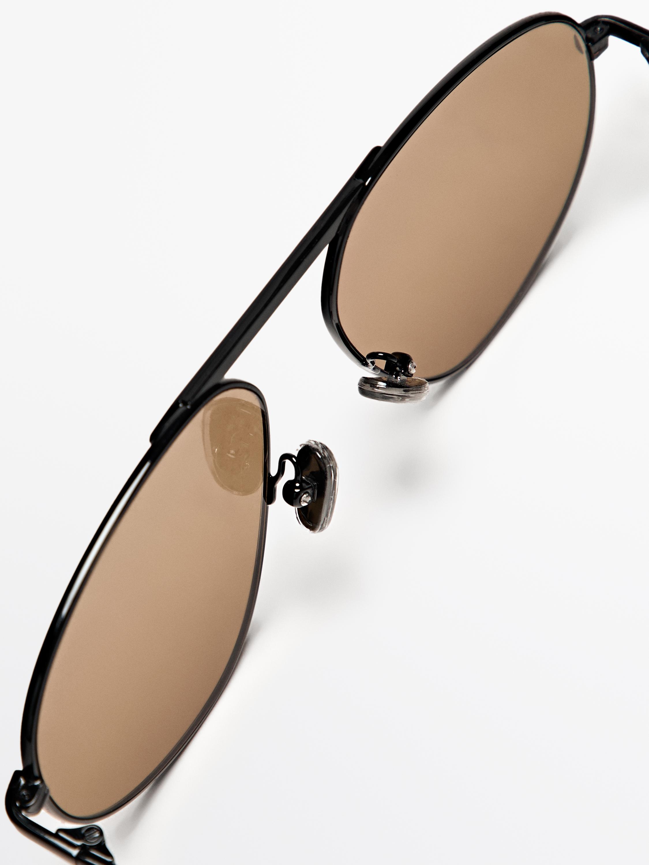 Détail de lunettes de soleil noires avec verres marron. Largeur verre : 58 mm, largeur pont : 15 mm, longueur branche : 148 mm.