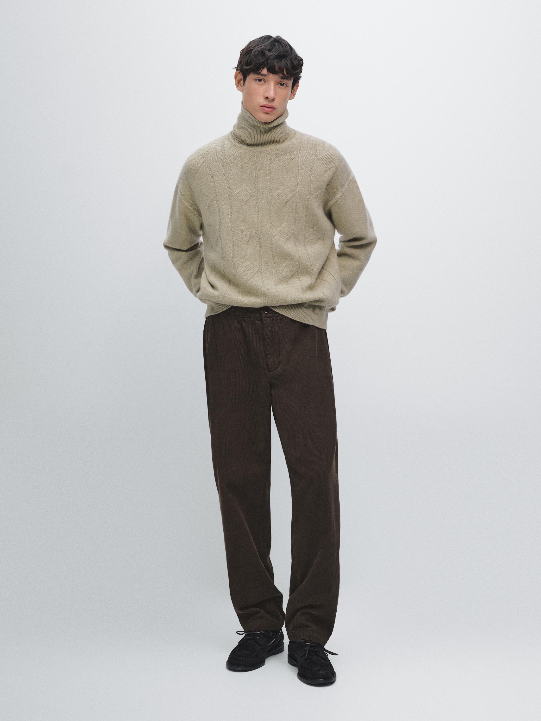 Conjunto de jersey beige de punto trenzado con cuello alto y pantalones marrones rectos.