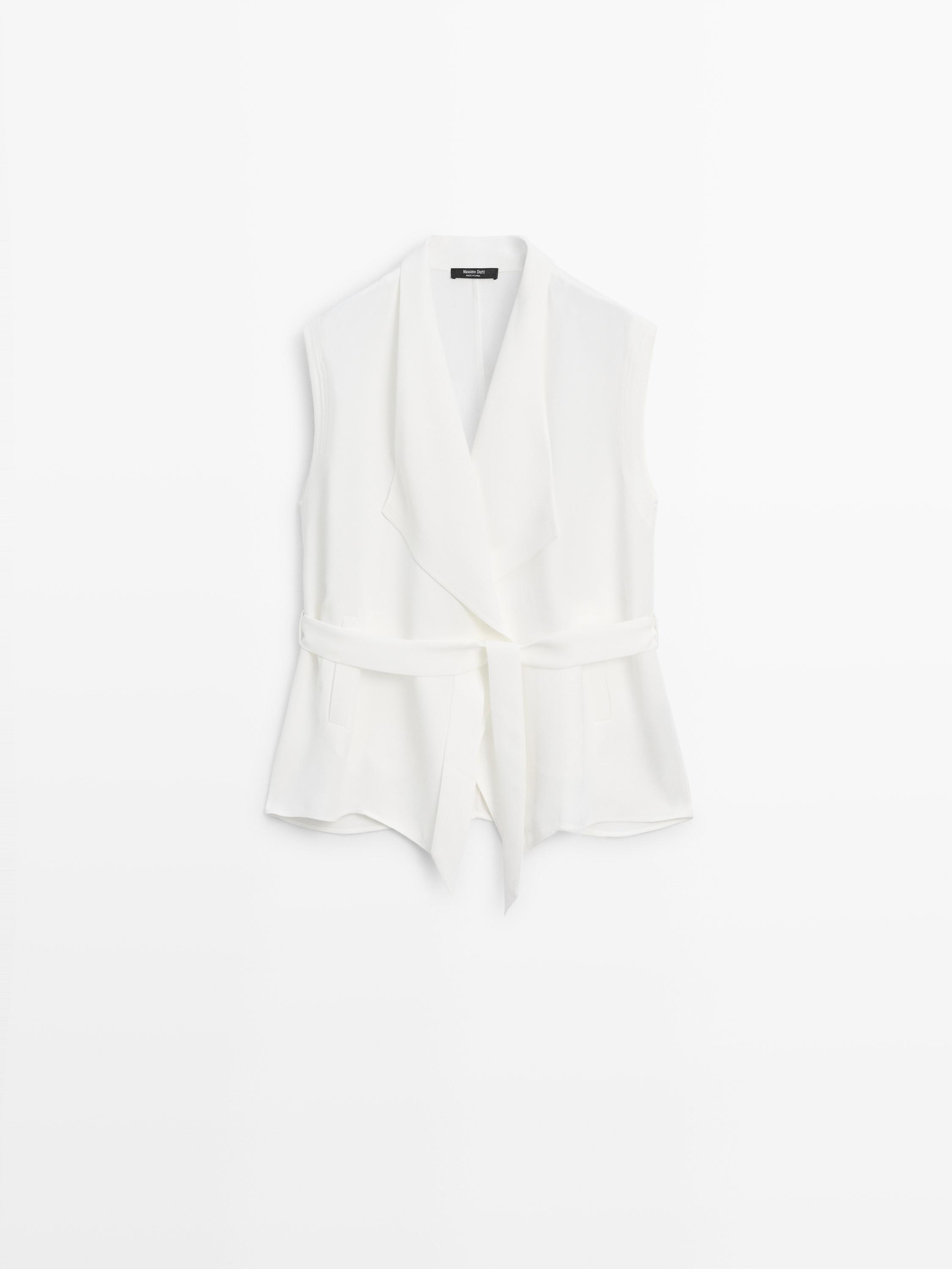 Tampilan depan rompi putih gading dengan kerah lebar, sabuk, dan saku samping.