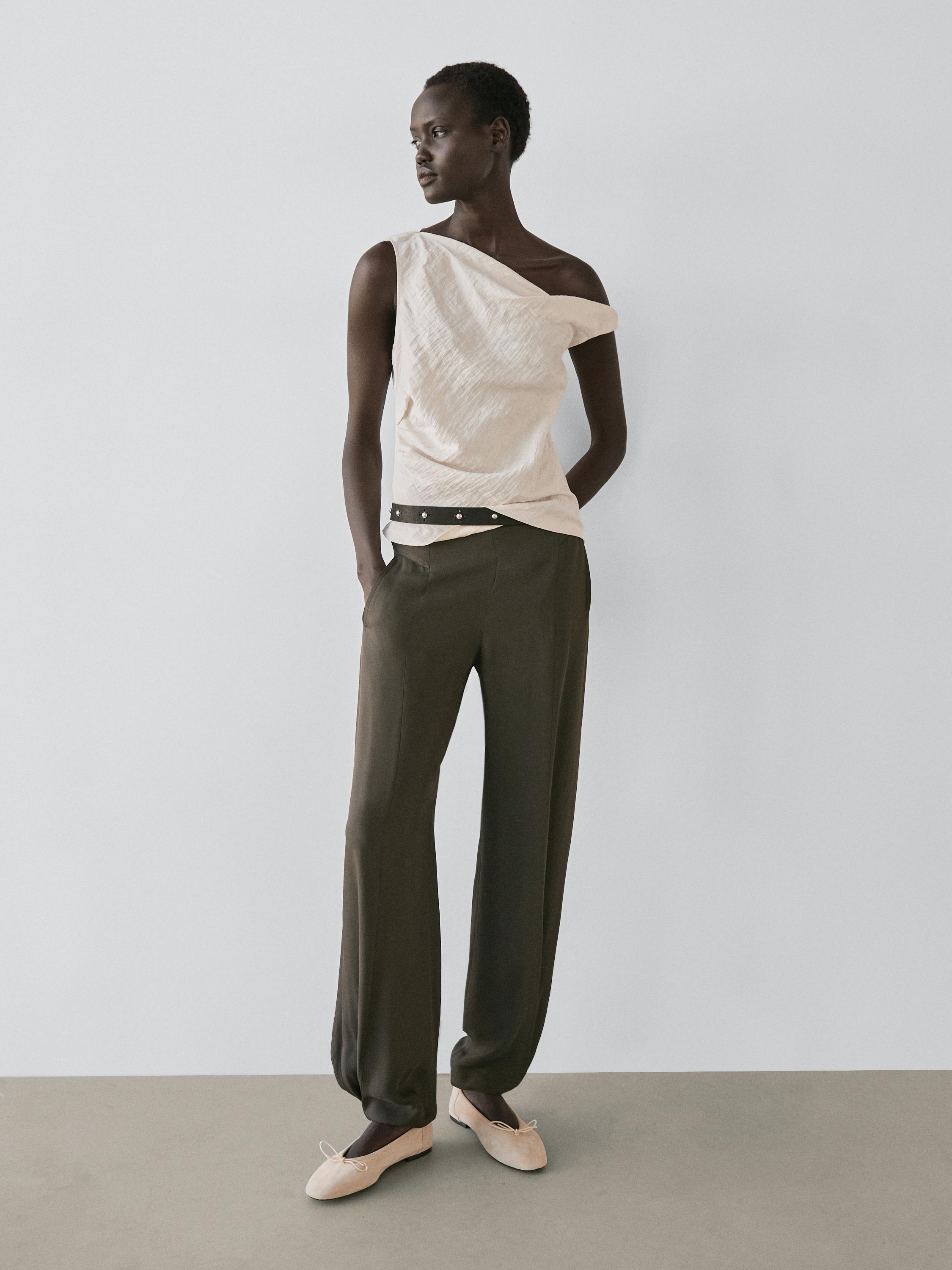 Conjunto de top bege assimétrico e calças verde-oliva de perna larga com cinto preto e sabrinas bege.