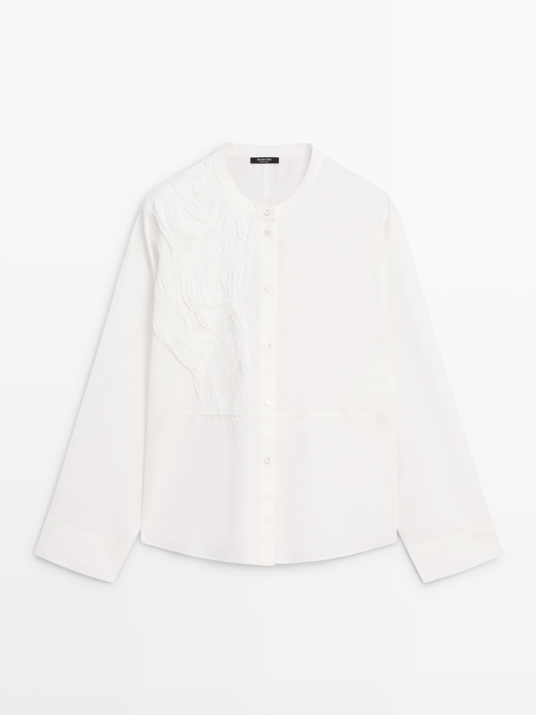 Sol omuzda nakışlı, yuvarlak yakalı ve ortadan düğmeli beyaz gömleğin önden görünümü.