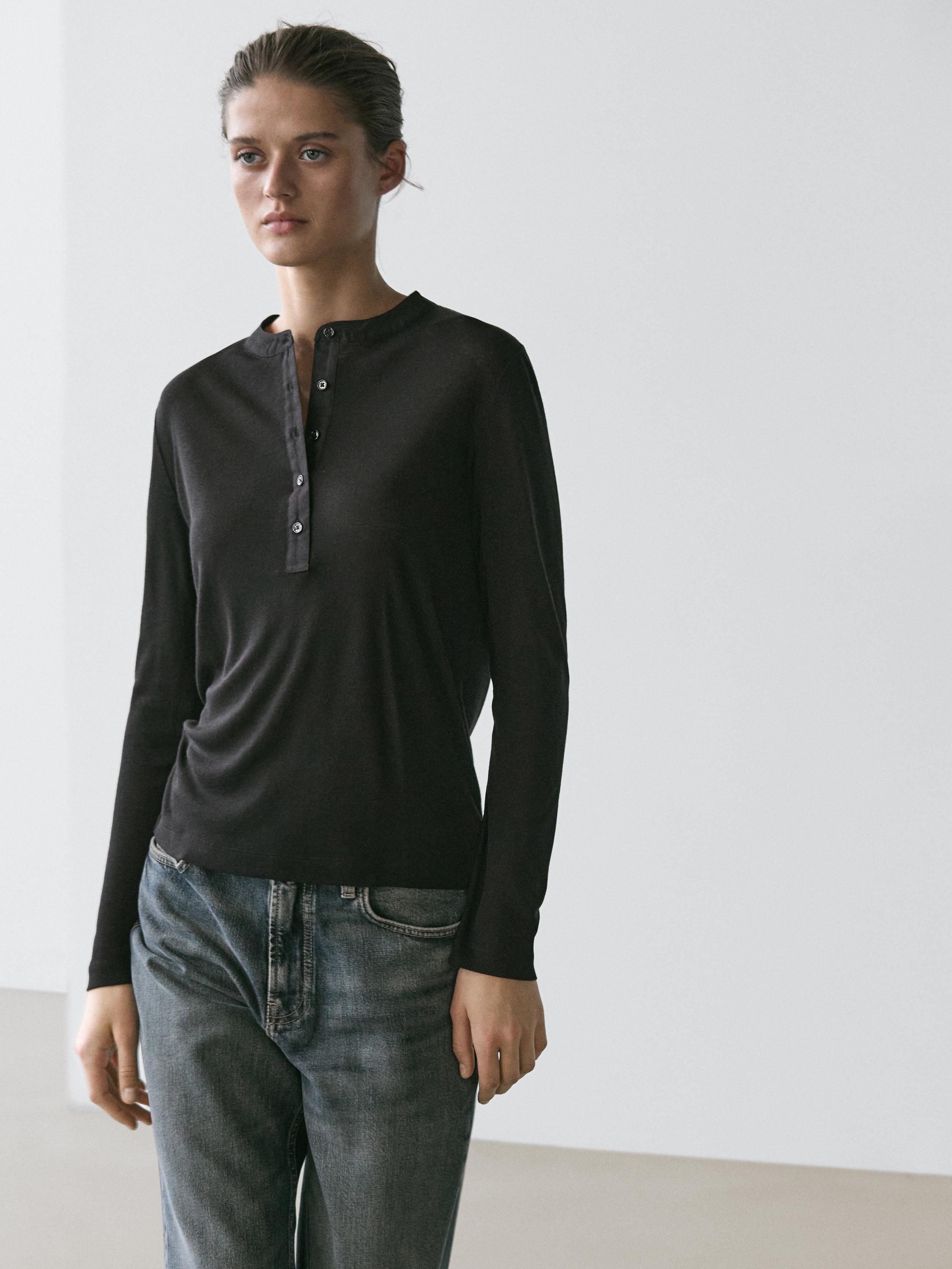 Black long-sleeve henley shirt and button set, paired with distressed blue jeans.
