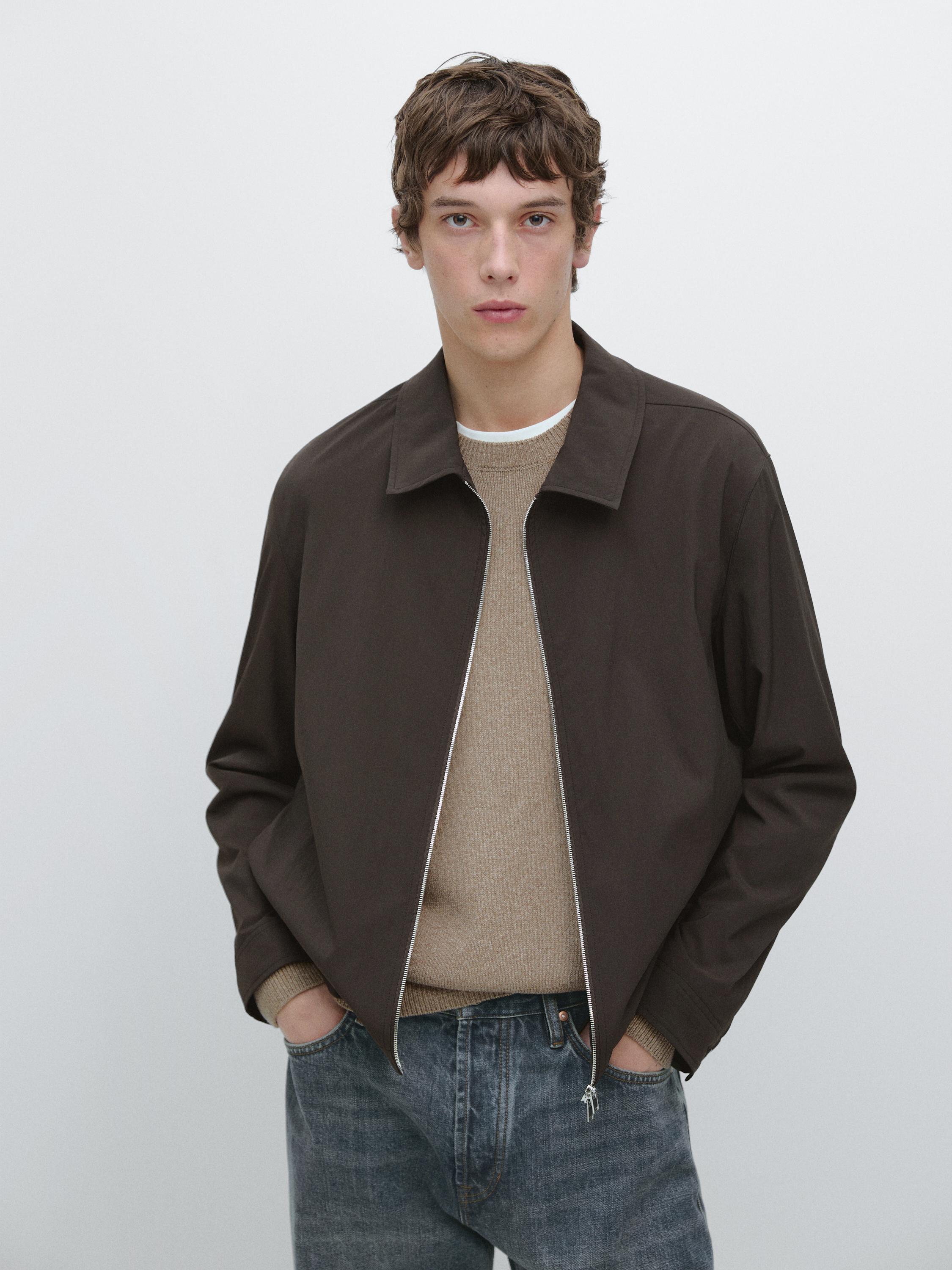 Braunes Jacken-Set mit Reißverschluss, beigem Pullover und blauen Jeans.