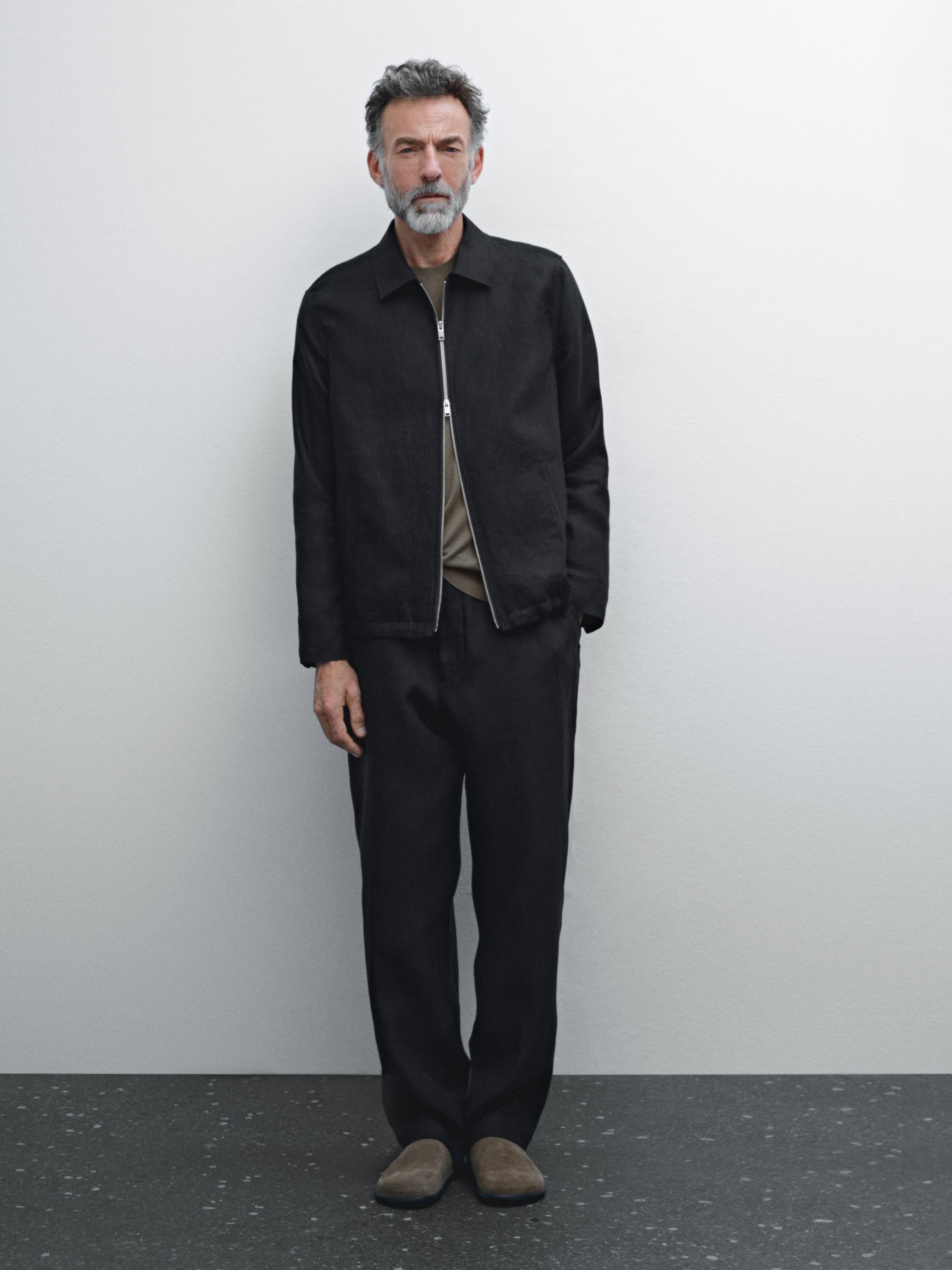 Ensemble veste noire zippée et pantalon noir avec t-shirt marron et chaussures beige.