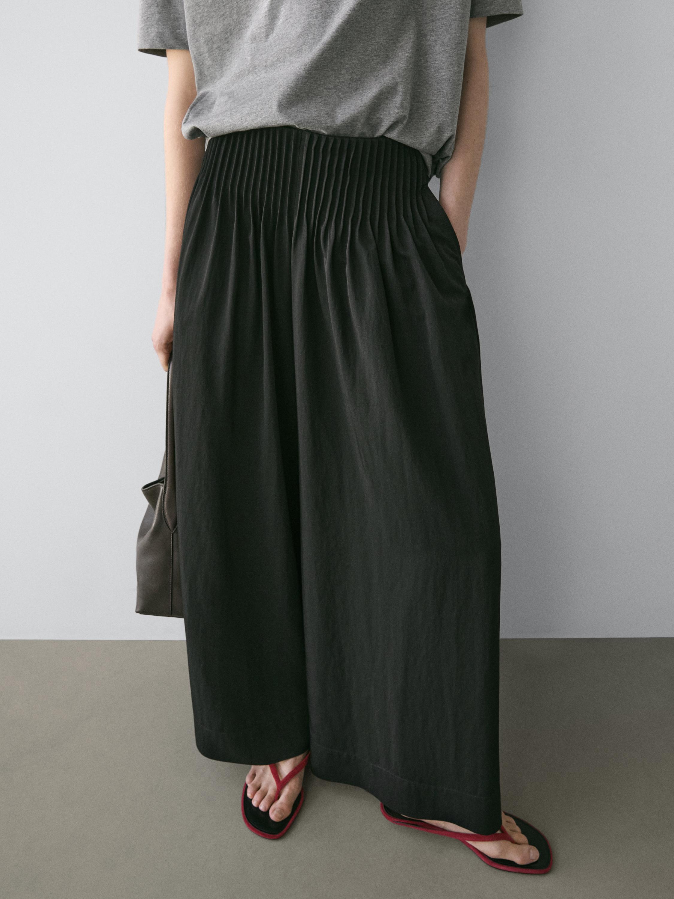 Medium shot of wide, flowing black pants with a ruched waist and side pockets.