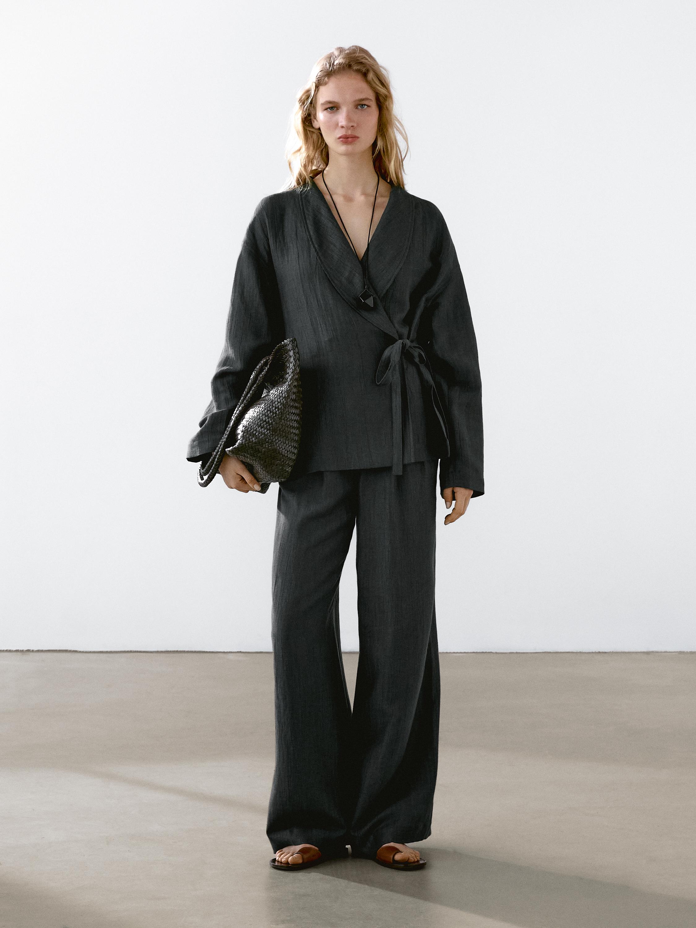 Conjunto de blusa negra cruzada con lazo y pantalones anchos a juego.