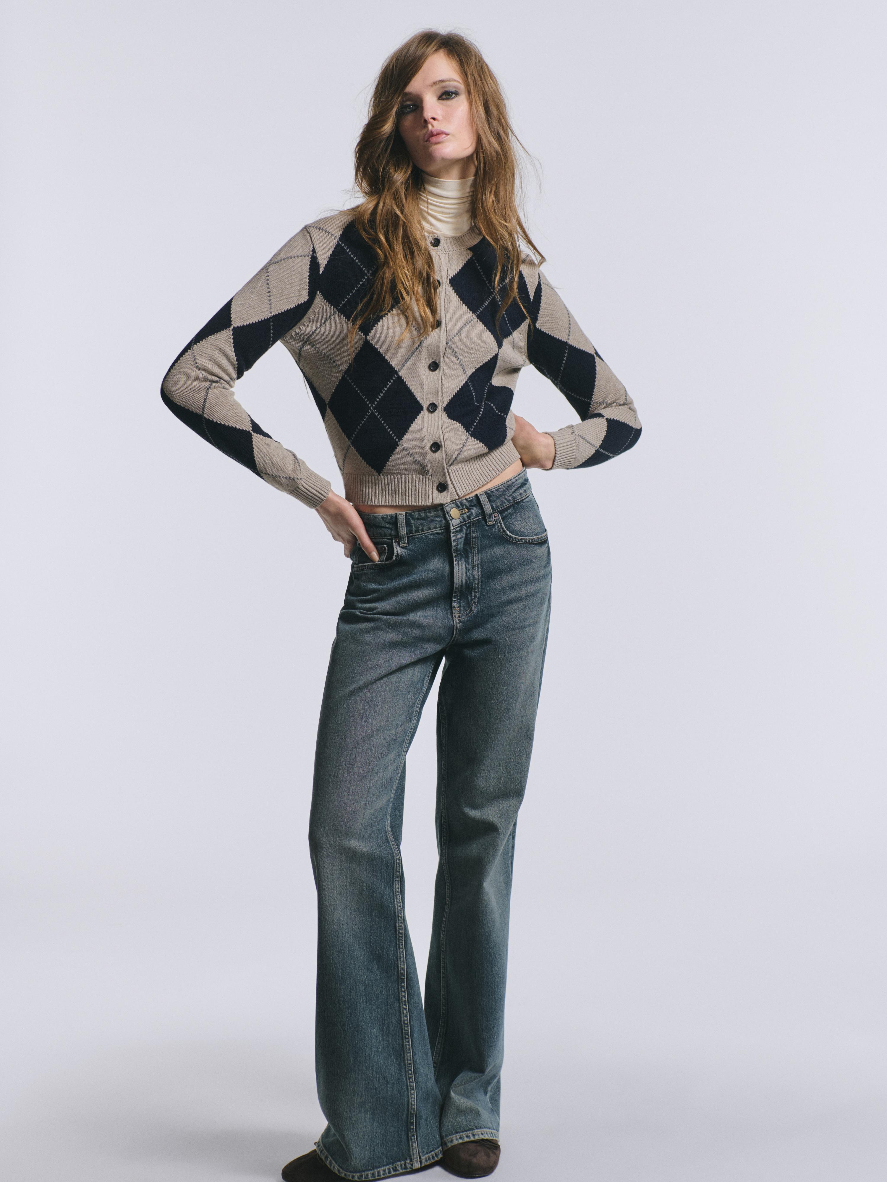 Navy blue argyle button-up cardigan set, beige turtleneck, and blue straight-leg jeans.