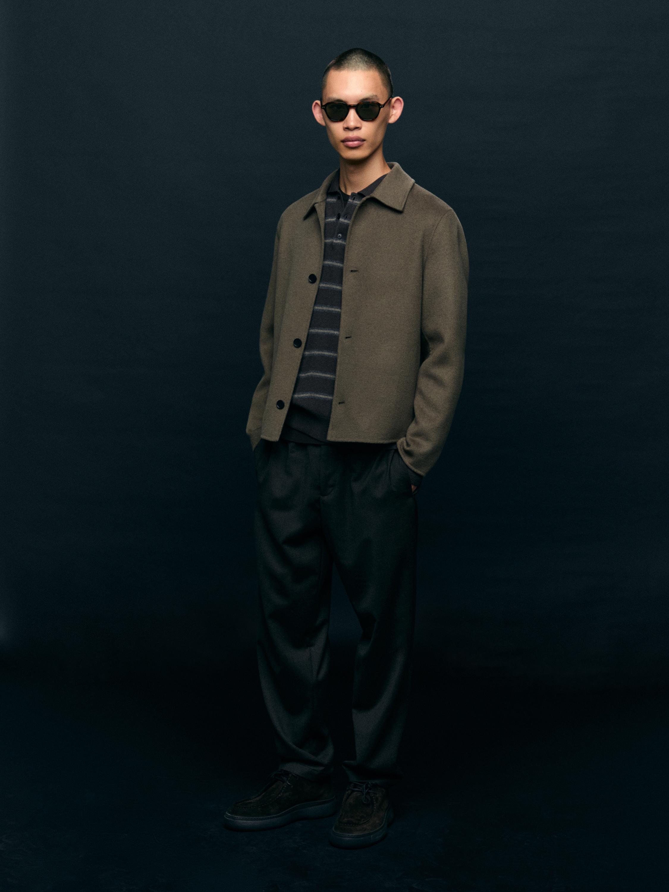 Комплект: коричневый пиджак на пуговицах, рубашка в серо-черную полоску, темные брюки и черные туфли.