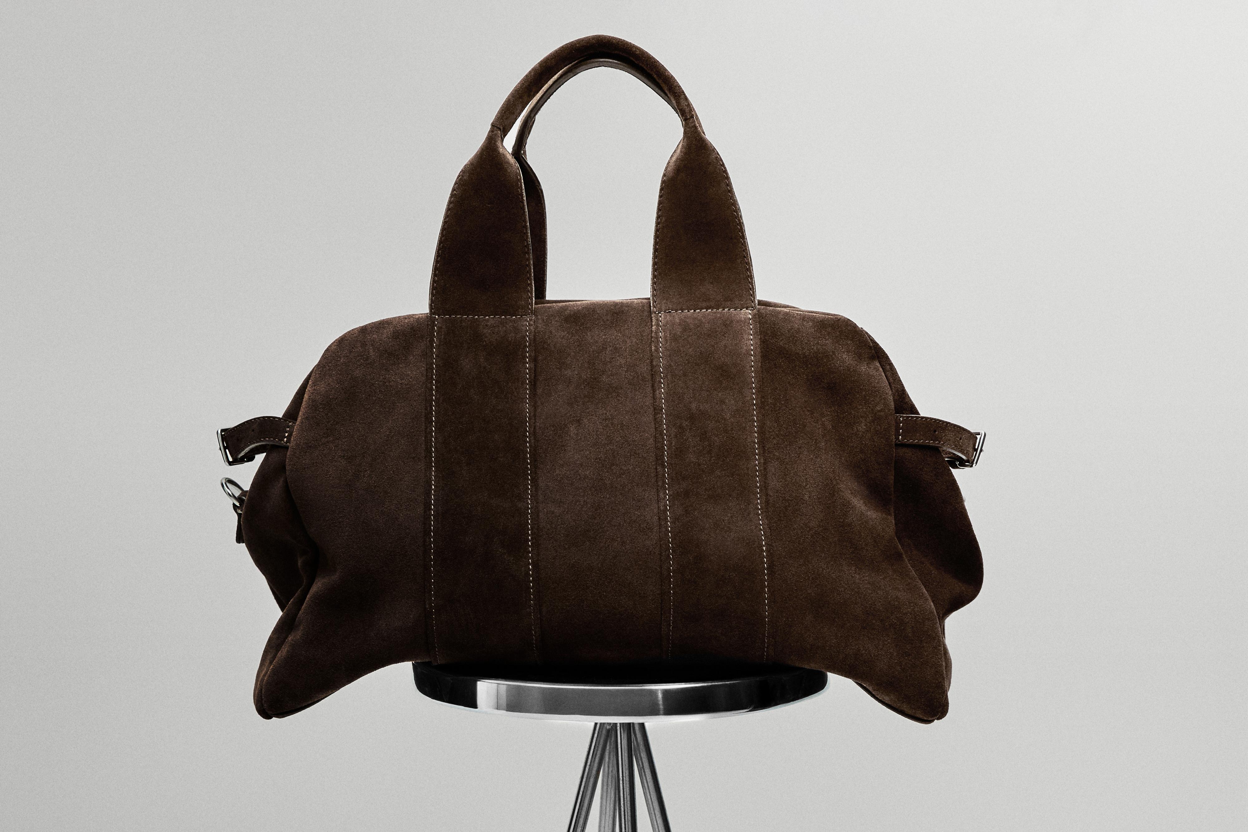 Topo koloreko poltsaren aurreko ikuspegia, helduleku bikoitzekin eta jostura bertikal ikusgarriekin, metalezko aulki baten gainean.