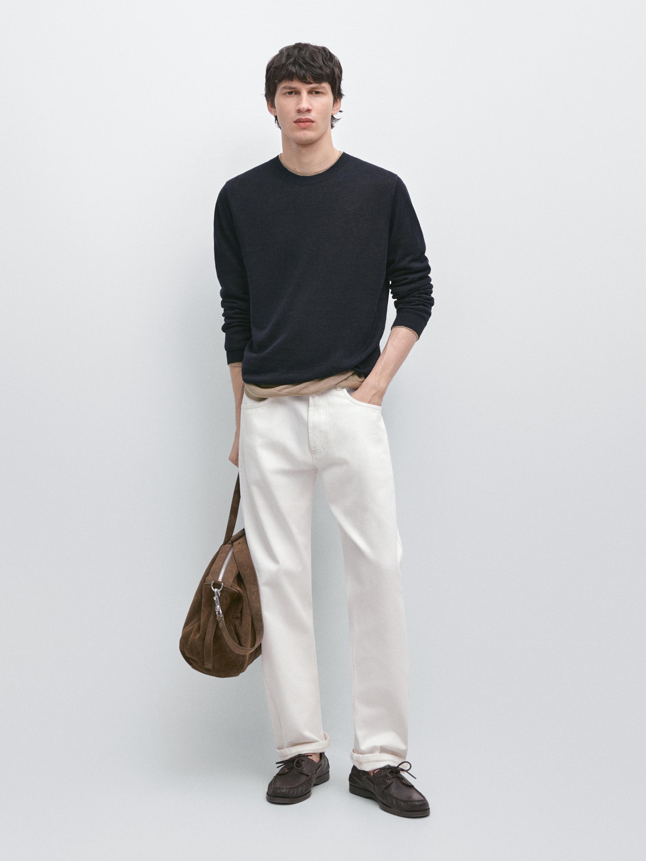 Conjunto de jersey azul marino de cuello redondo y pantalones blancos rectos. Lleva bolso marrón y zapatos oscuros.