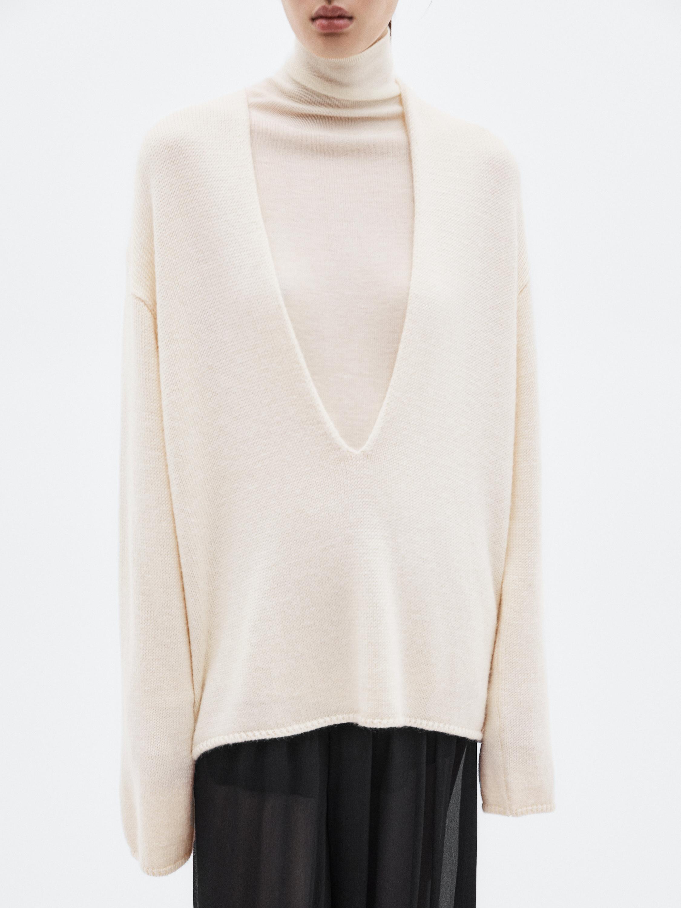 Mid-shot of a beige sweater with a deep V-neck, over a beige turtleneck.