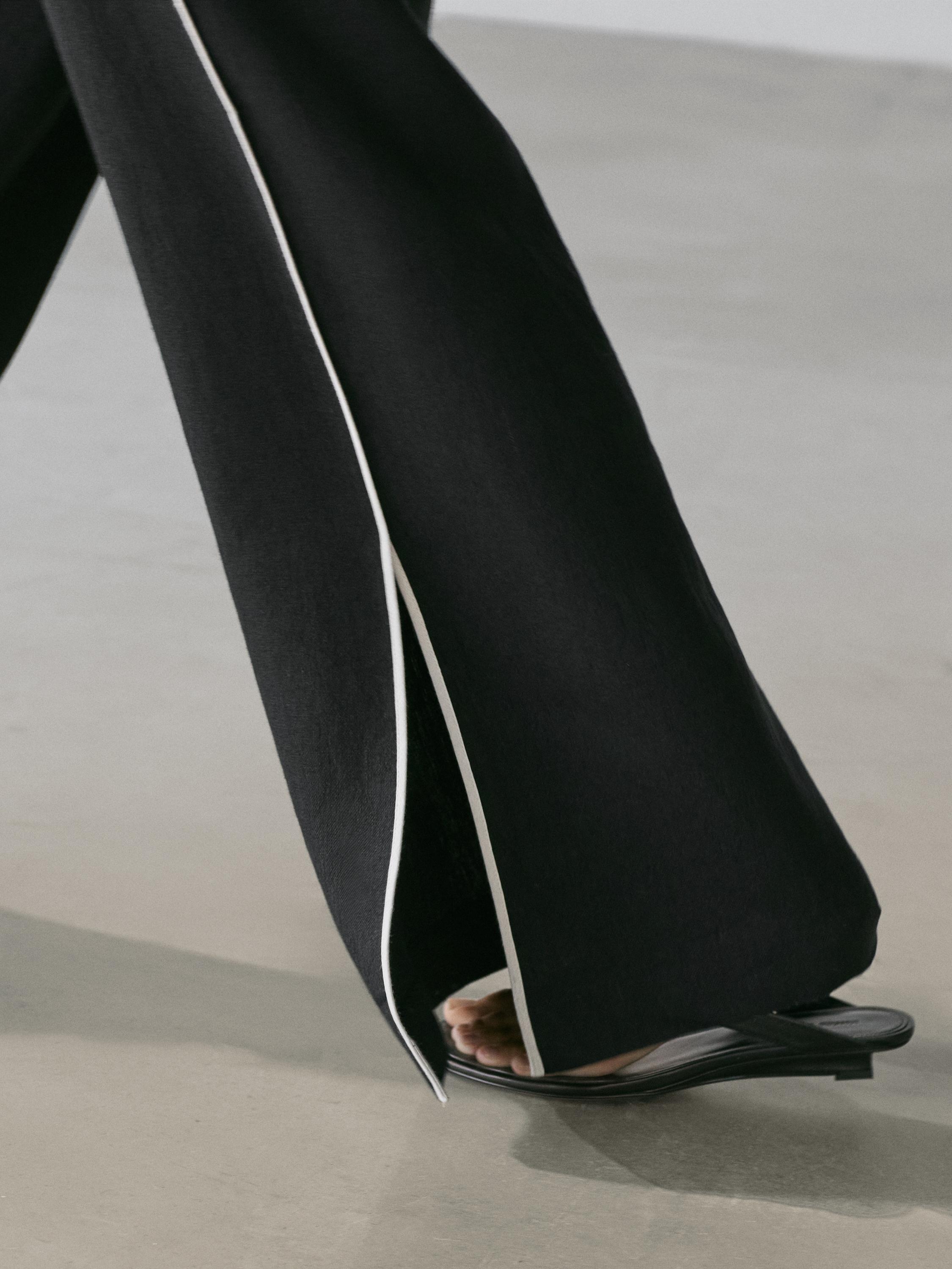 Detalle de pantalón negro con vivo blanco y abertura lateral.