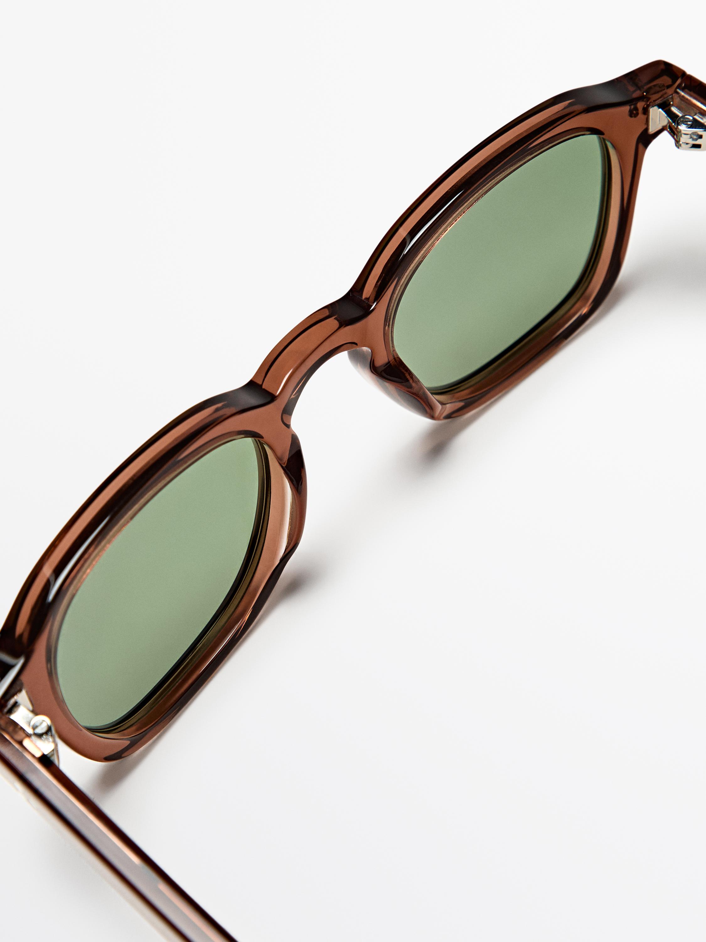 Primer plano de gafas de sol marrón jaspeado con lentes verdes y armazón grueso rectangular.