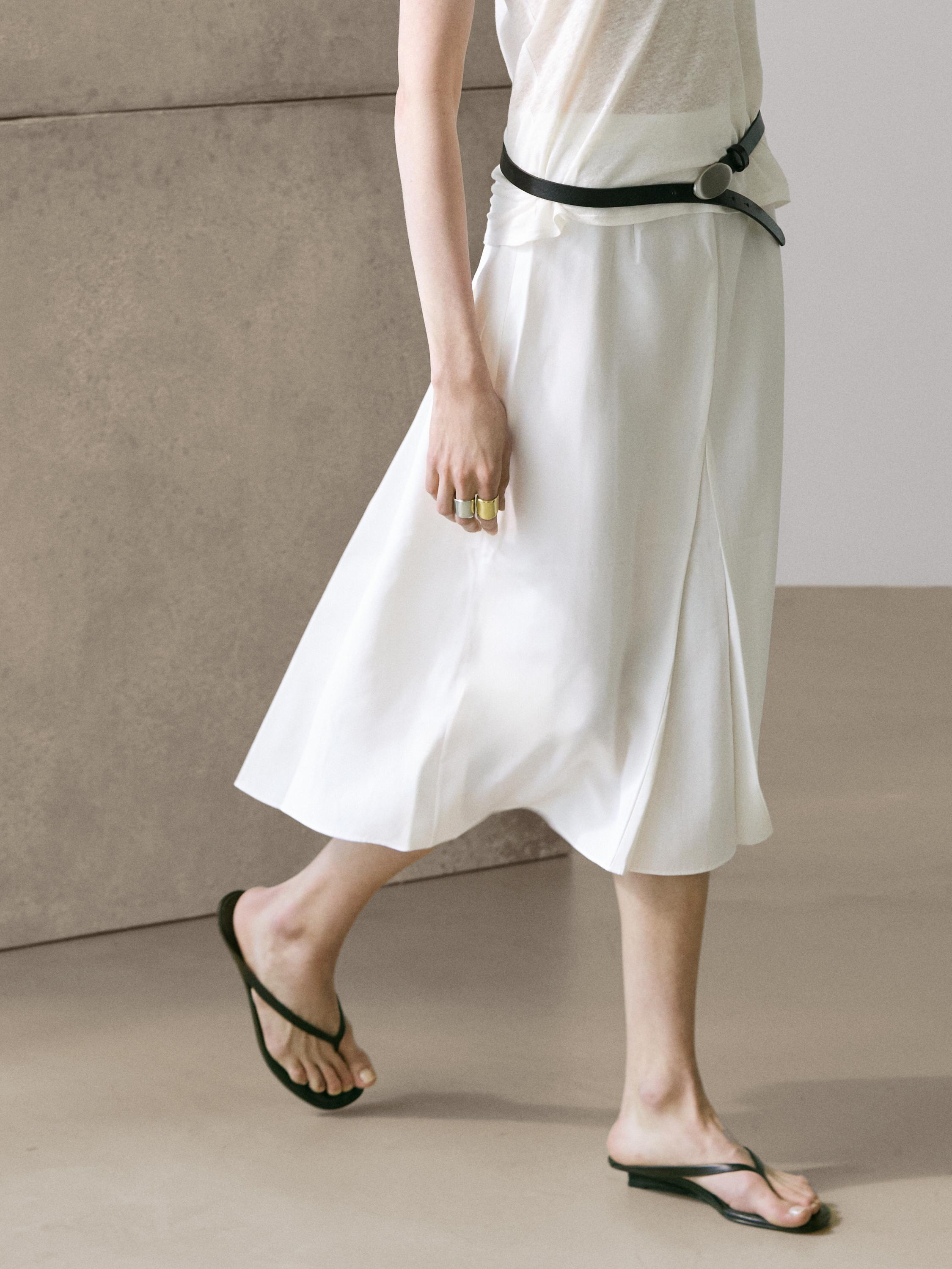 plaintext Mid-shot van witte midi-rok met plooien en zwarte riem.