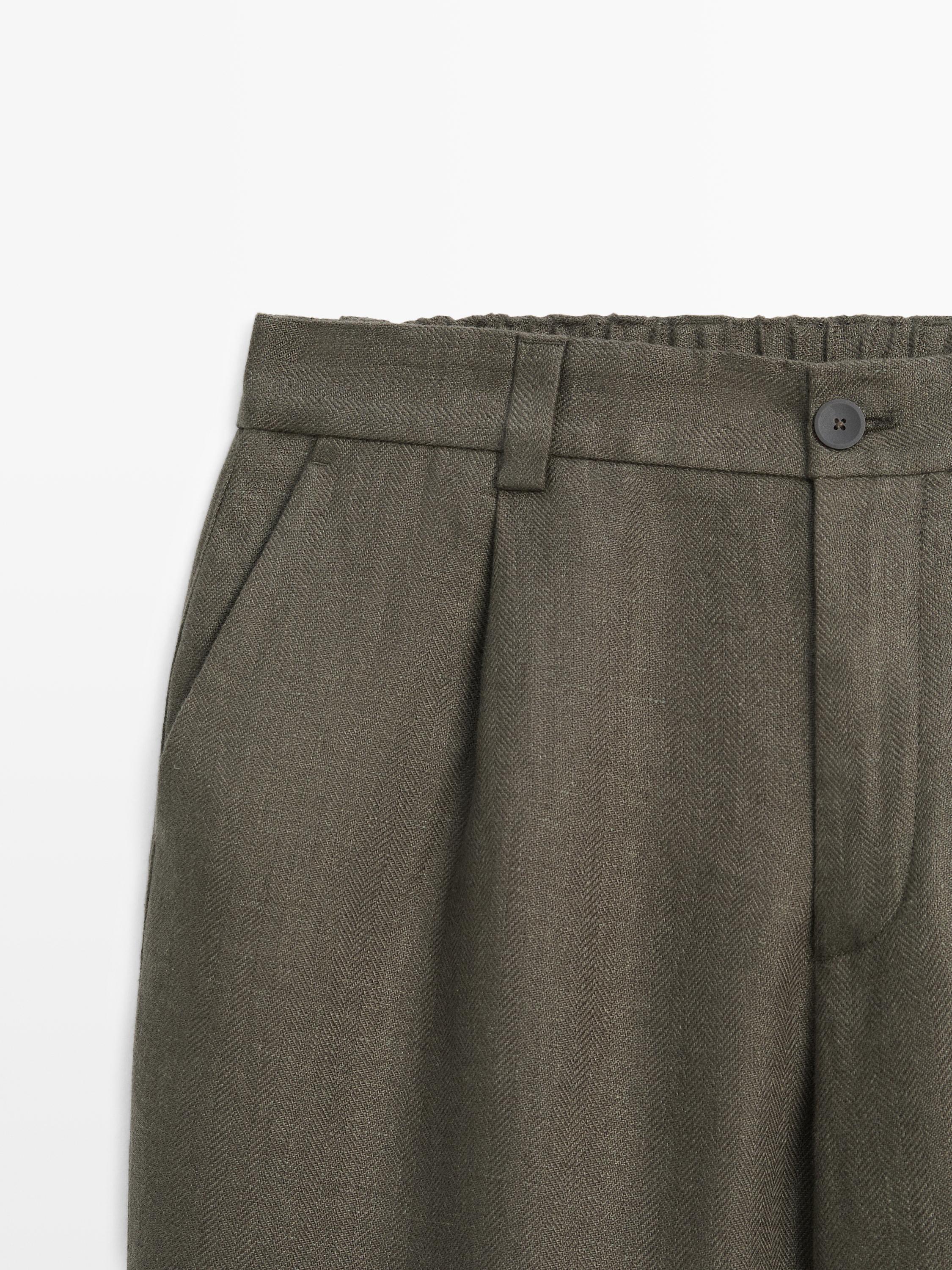 Μεσαίο πλάνο πράσινου παντελονιού με λεπτομέρεια ψαροκόκαλο, ελαστική μέση, μπροστινό κουμπί και πλαϊνές τσέπες.