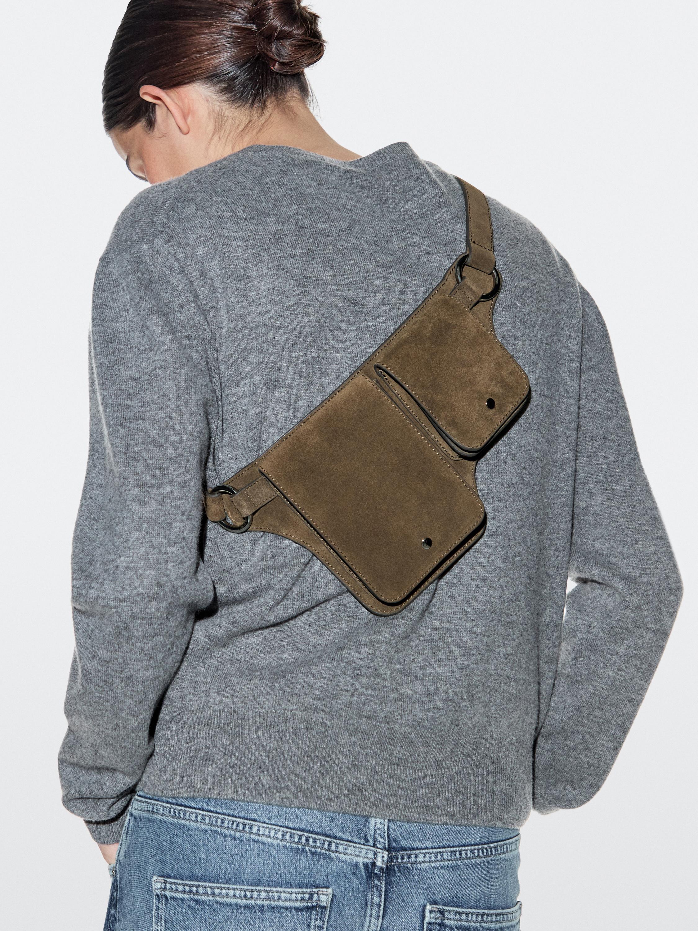 Double-compartment khaki fanny pack set visible over a gray sweater and blue jeans.