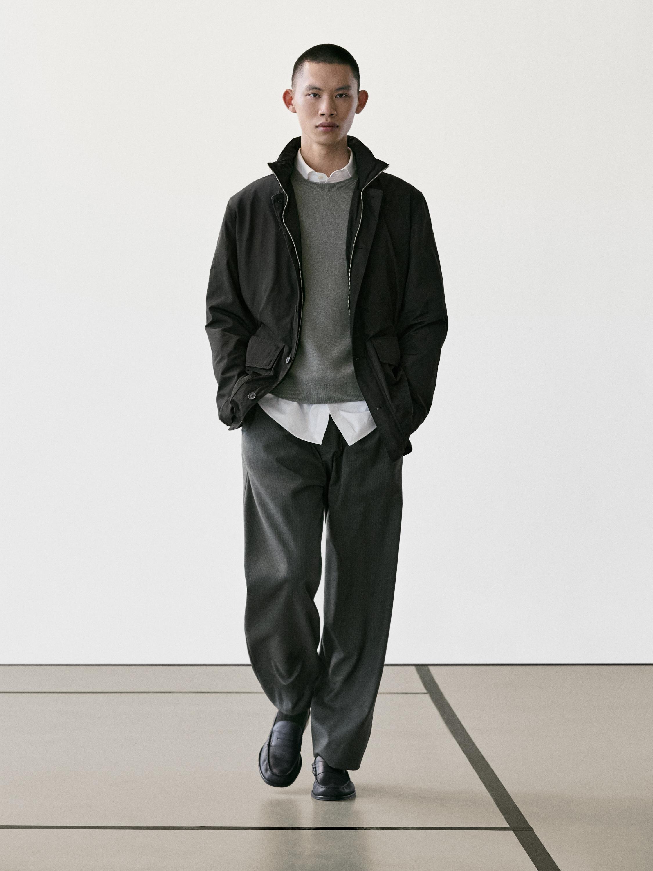 ชุดเสื้อแจ็คเก็ตสีดำมีกระเป๋า, เสื้อสเวตเตอร์สีเทา, เสื้อเชิ้ตสีขาว, กางเกงขายาวสีเทาทรงหลวม และรองเท้าสีดำ