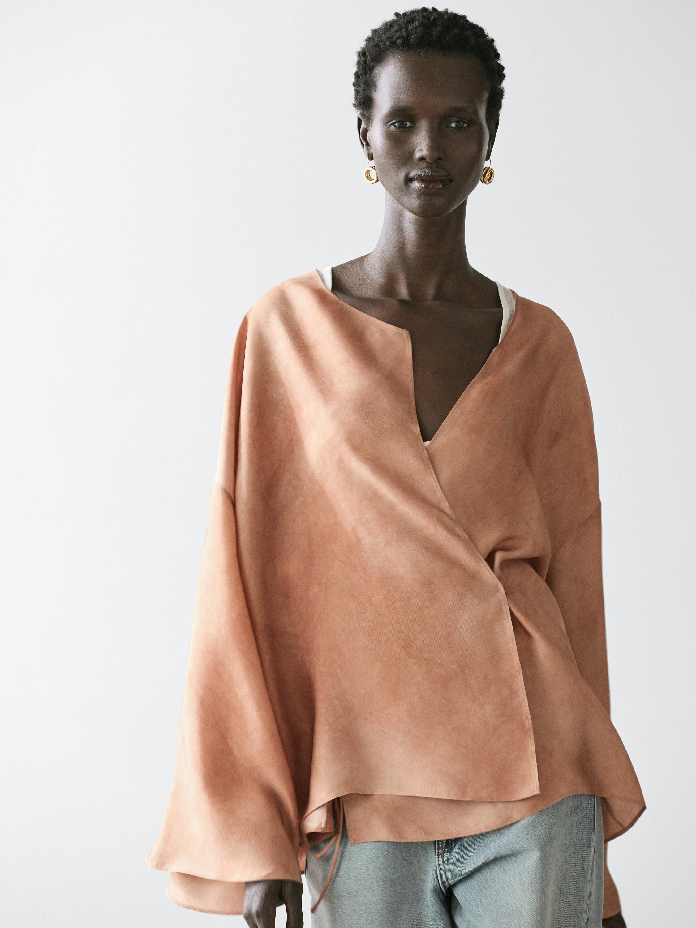 Plano medio de blusa fluida cruzada beige con mangas amplias y escote en V, combinada con jeans claros.