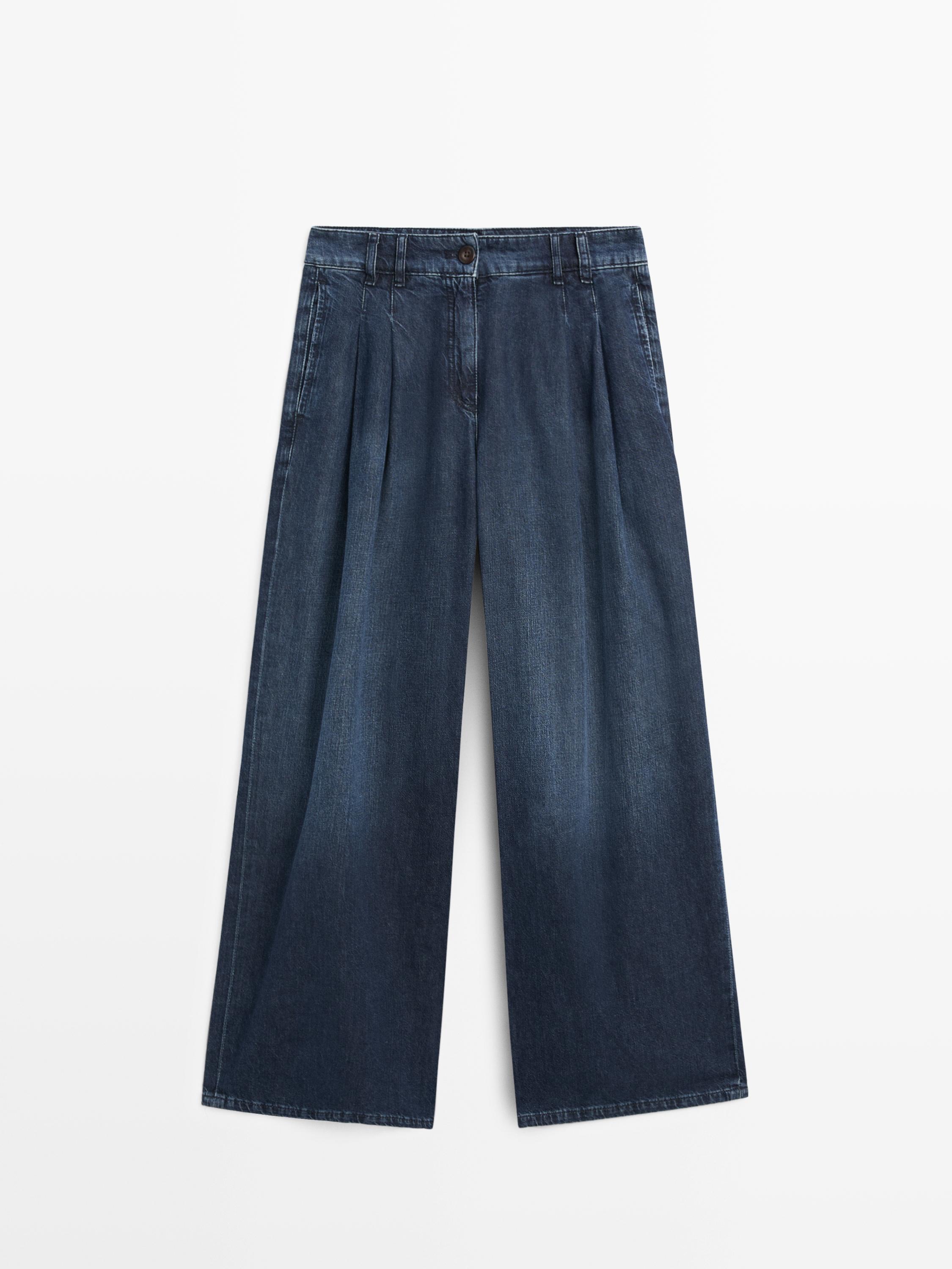 Vooraanzicht van donkerblauwe, wijdvallende jeans met plooien en hoge taille, zijzakken en knoopsluiting.