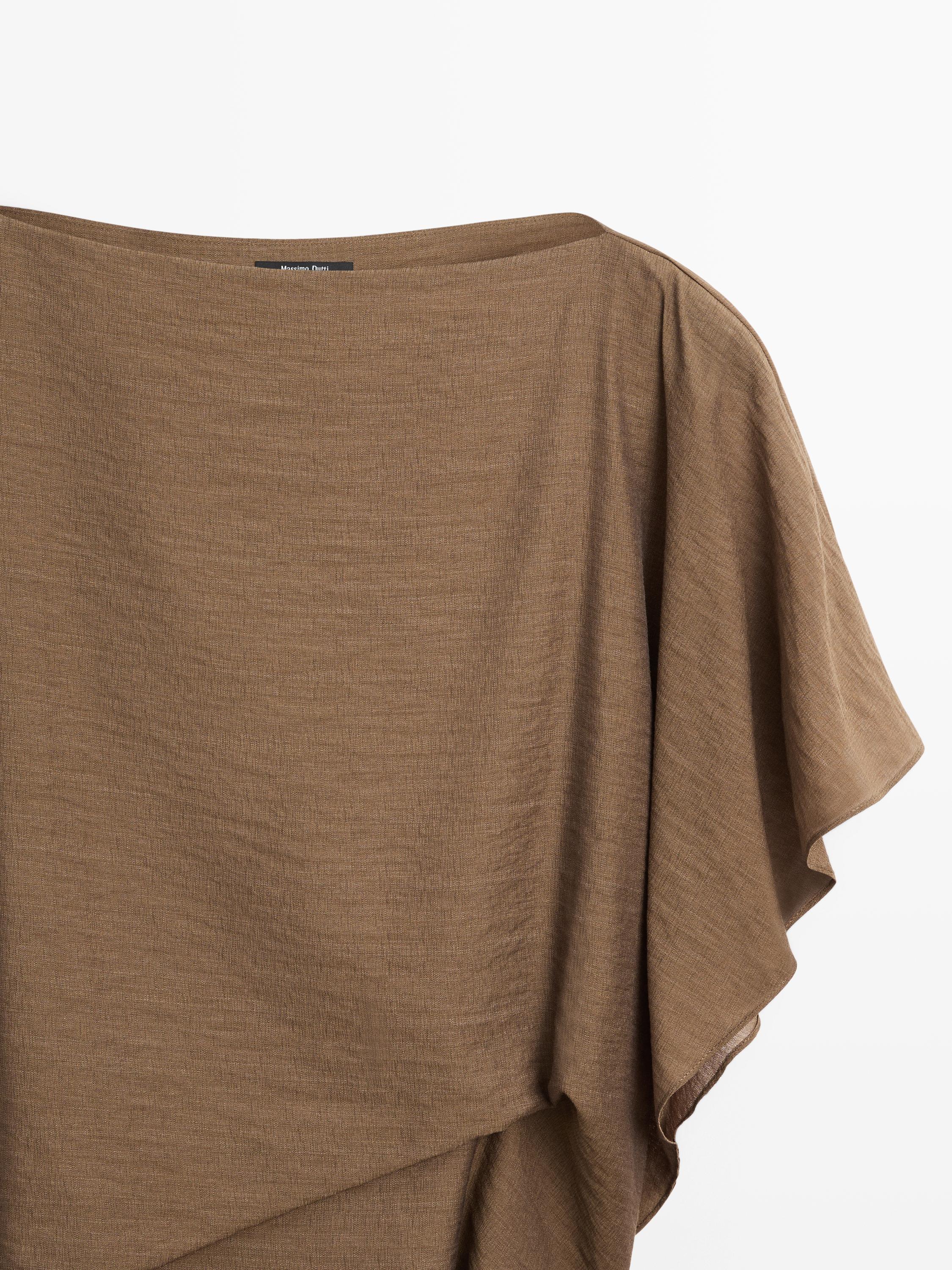 "Detail of the top of a khaki shirt with a round neck and wide sleeves."