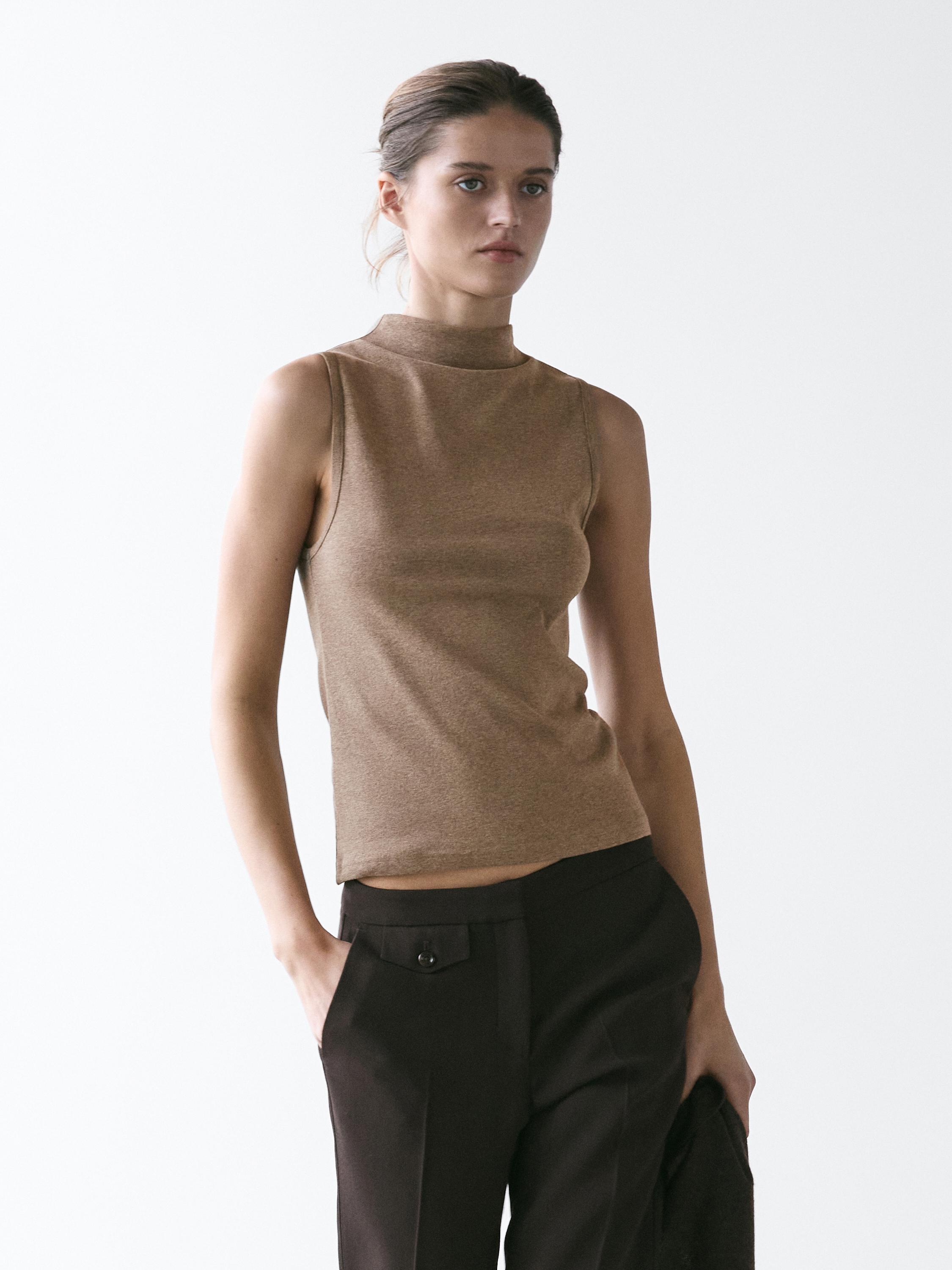 Conjunto de top sin mangas color visón con cuello chimenea y pantalón oscuro con bolsillos laterales.