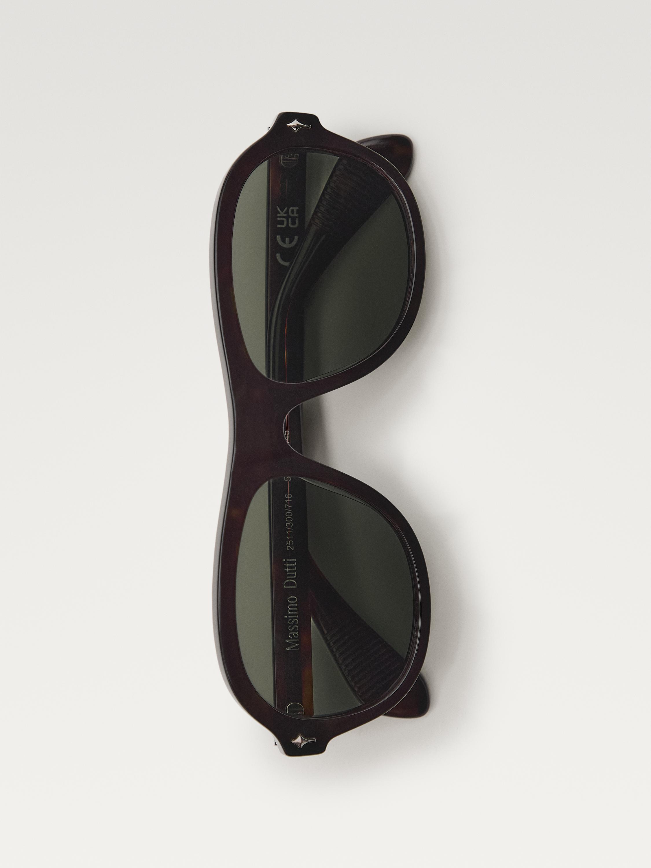 Oval çerçeveli ve koyu renk camlı kahverengi güneş gözlüğü. Görünen metin: "Massimo Dutti", "UK CA".