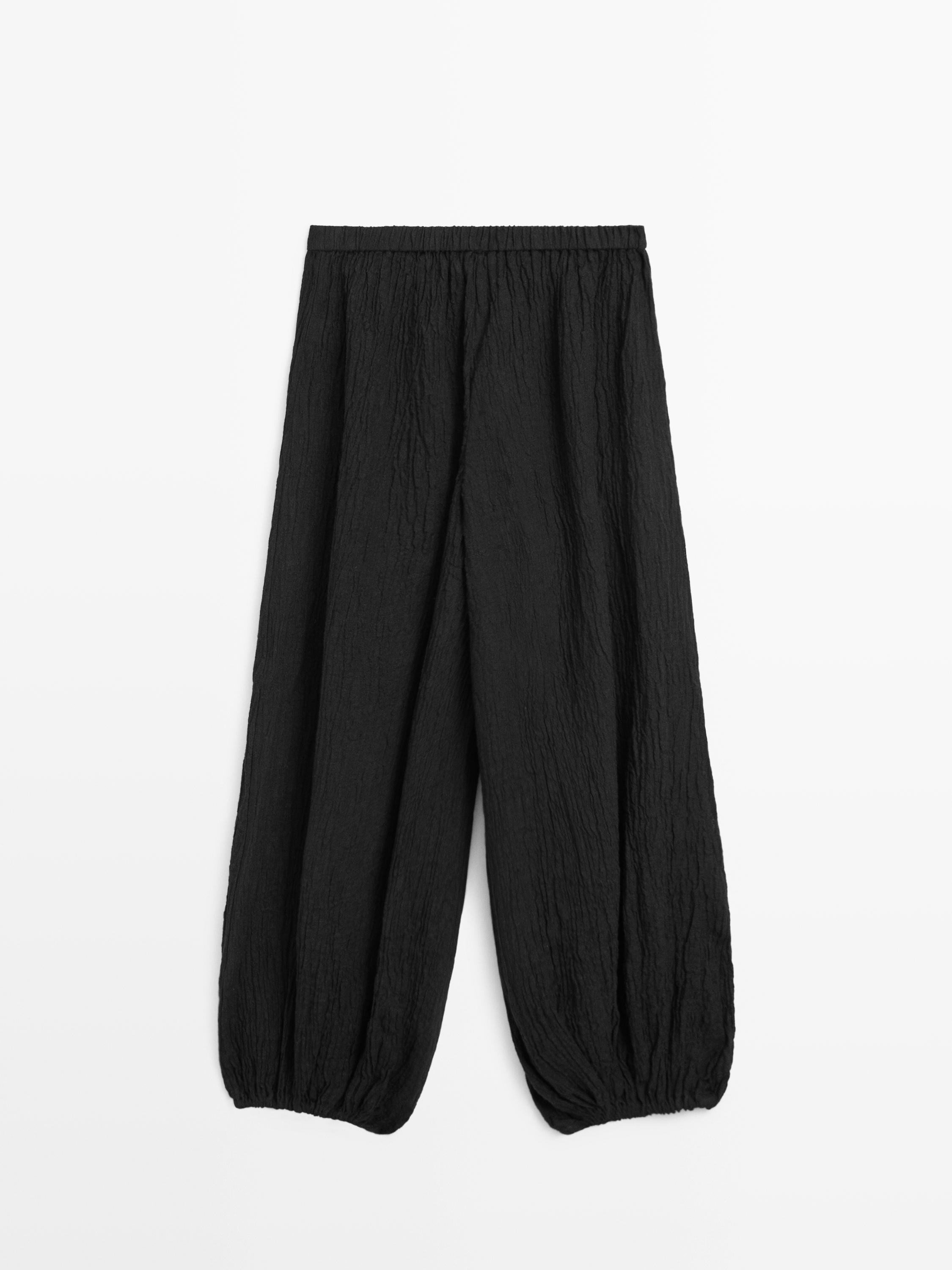 Vooraanzicht van een zwarte broek met elastische taille en geplooide wijde pijpen bij de enkels.