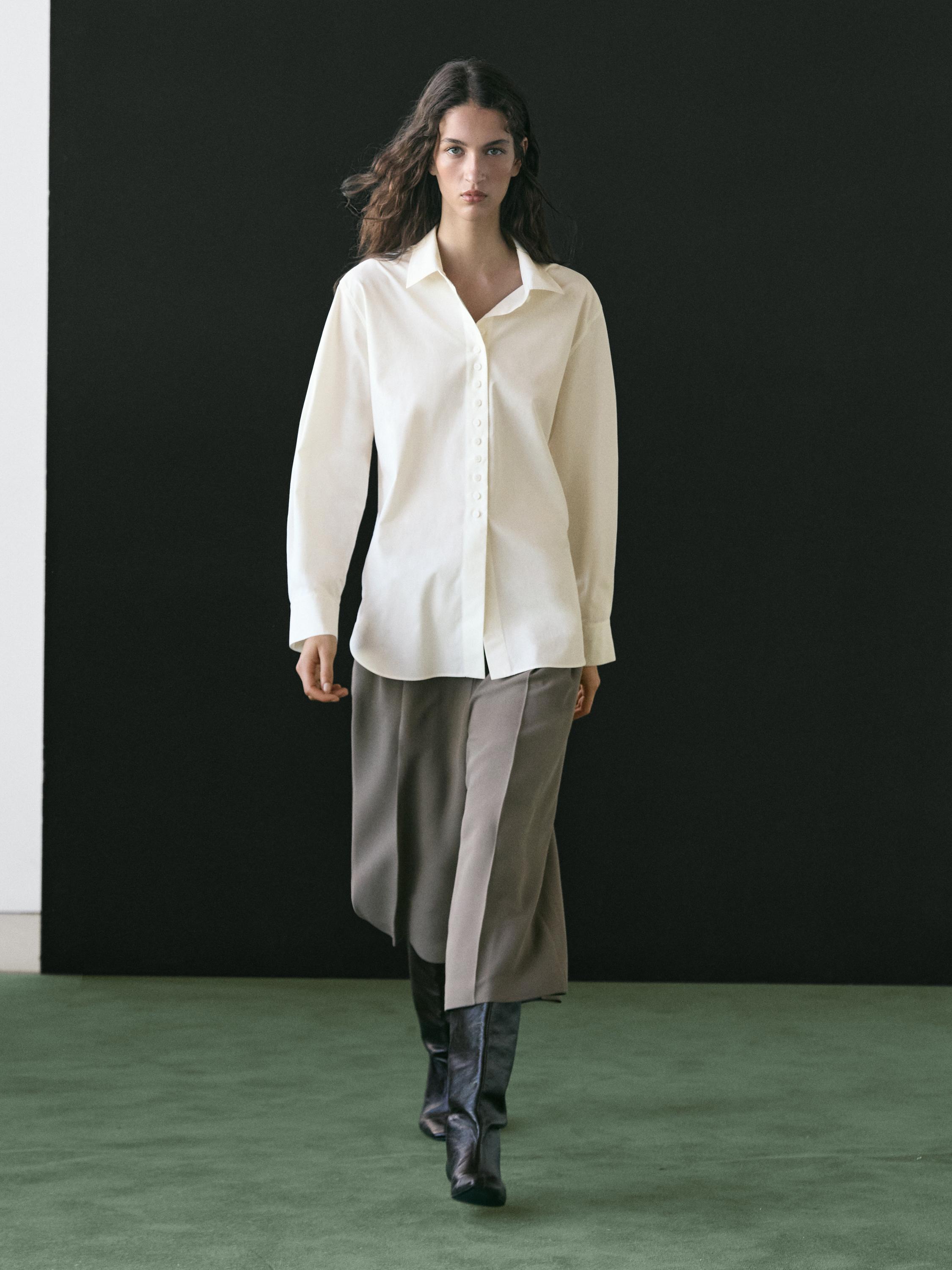 Conjunto de camisa blanca con botones y pantalones anchos grises, combinado con botas altas negras.