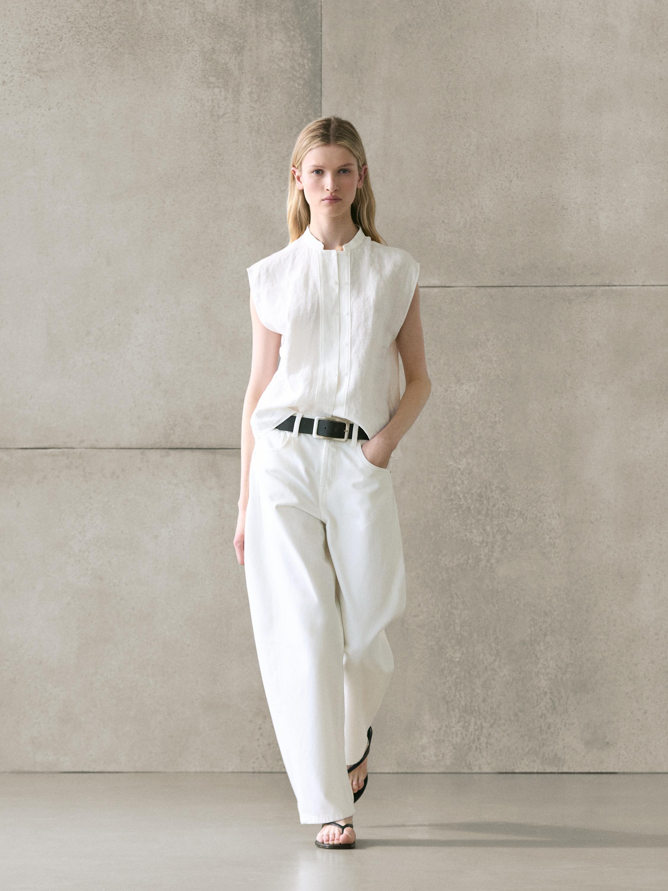 Conjunto de camisa blanca sin mangas con botonadura frontal y pantalones anchos blancos con cinturón negro.