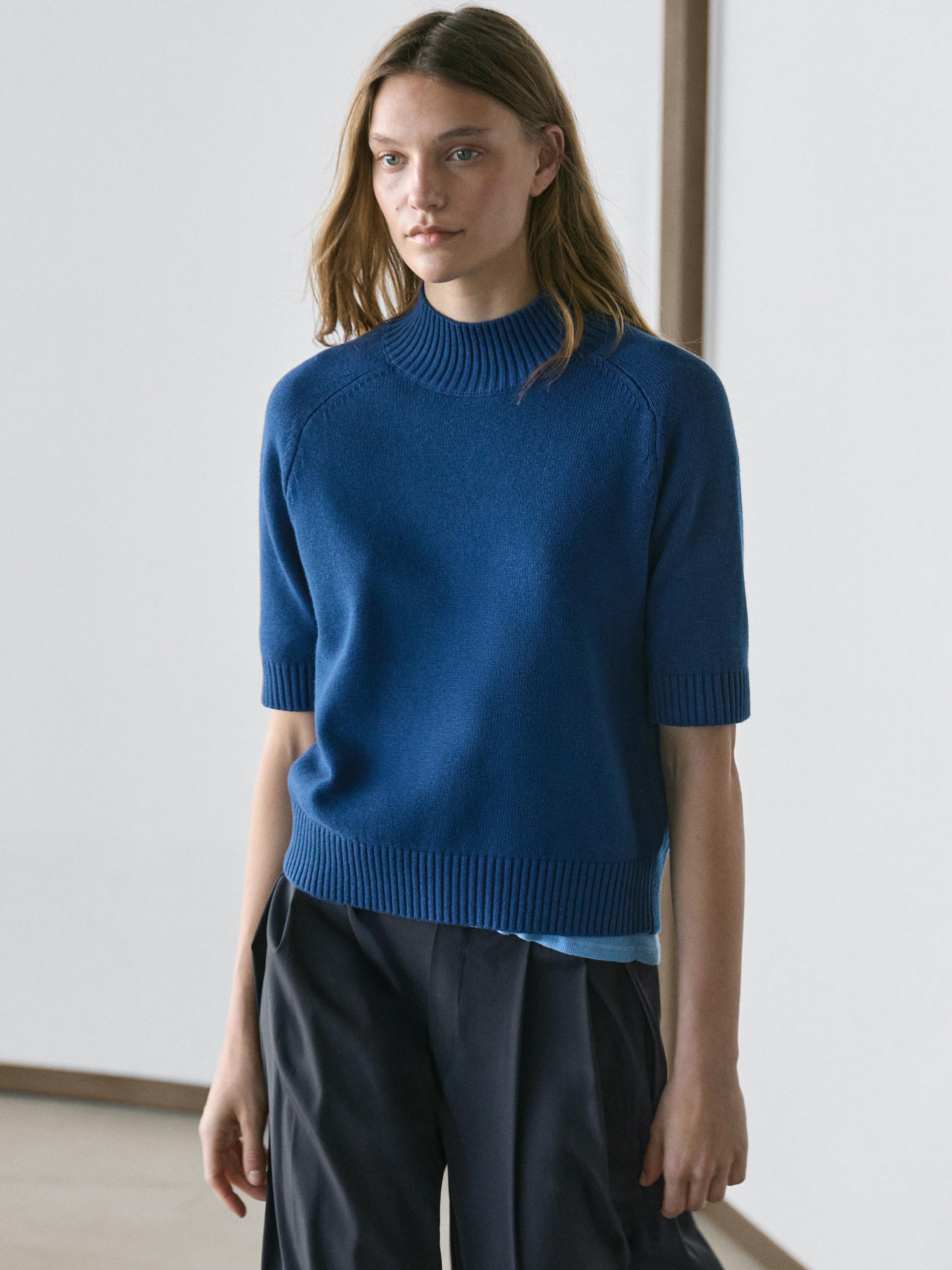 Ensemble composé d'un pull bleu foncé à manches courtes et col roulé côtelé, associé à un pantalon foncé.
