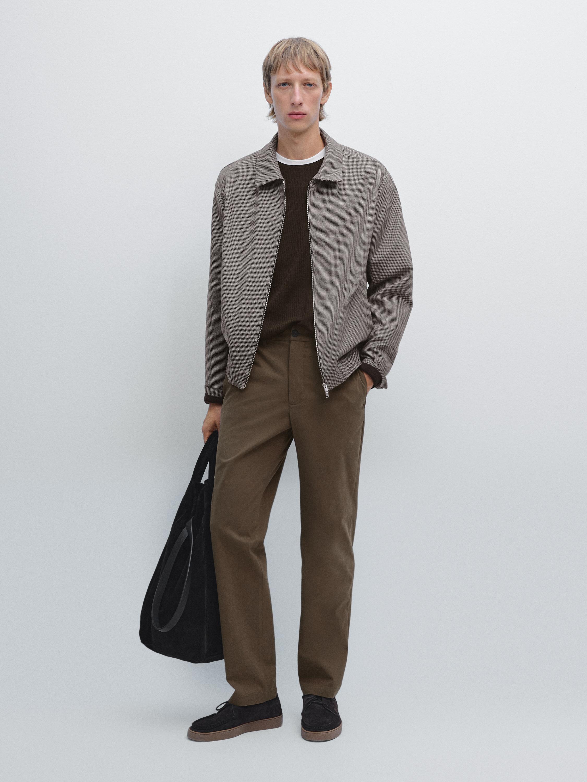 Outfit consisting of a gray jacket, brown t-shirt, brown casual pants, and black shoes. She's carrying a black purse.