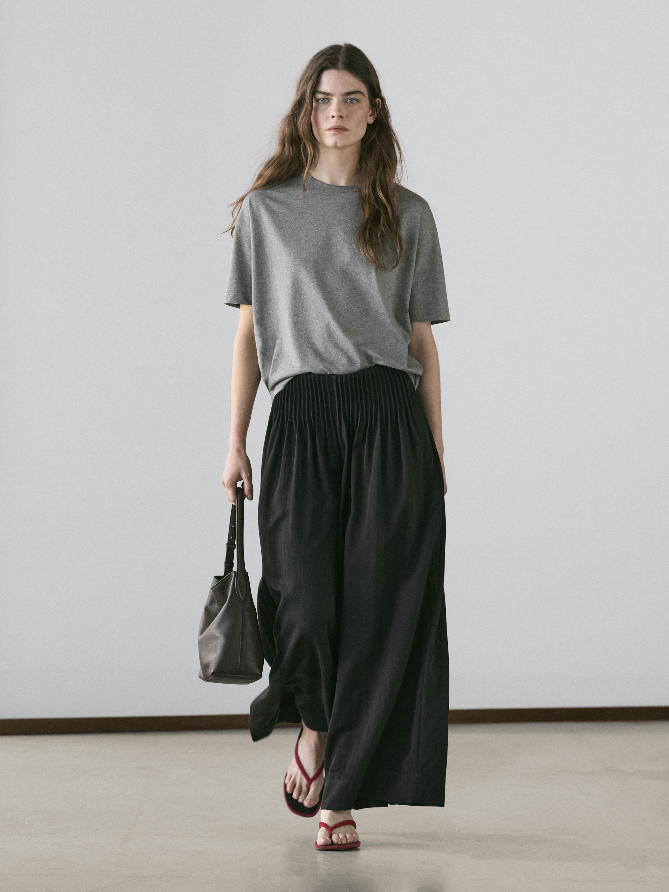 Gray t-shirt and wide-leg black pants set, with red sandals and a black bag.