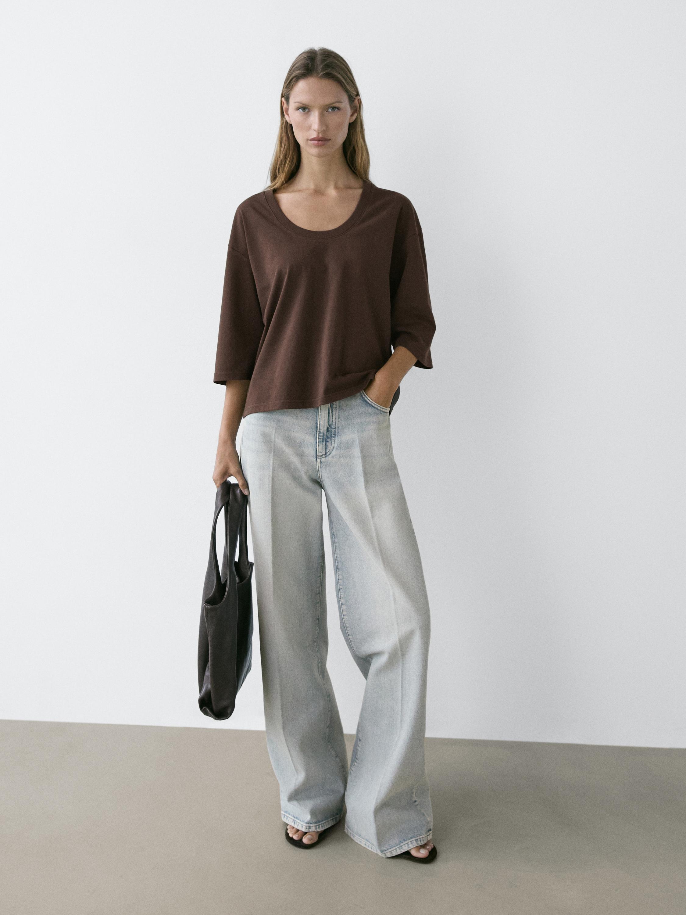 Zestaw składający się z brązowej koszulki z krótkim rękawem i okrągłym dekoltem, jasnych szerokich jeansów oraz czarnej torebki.