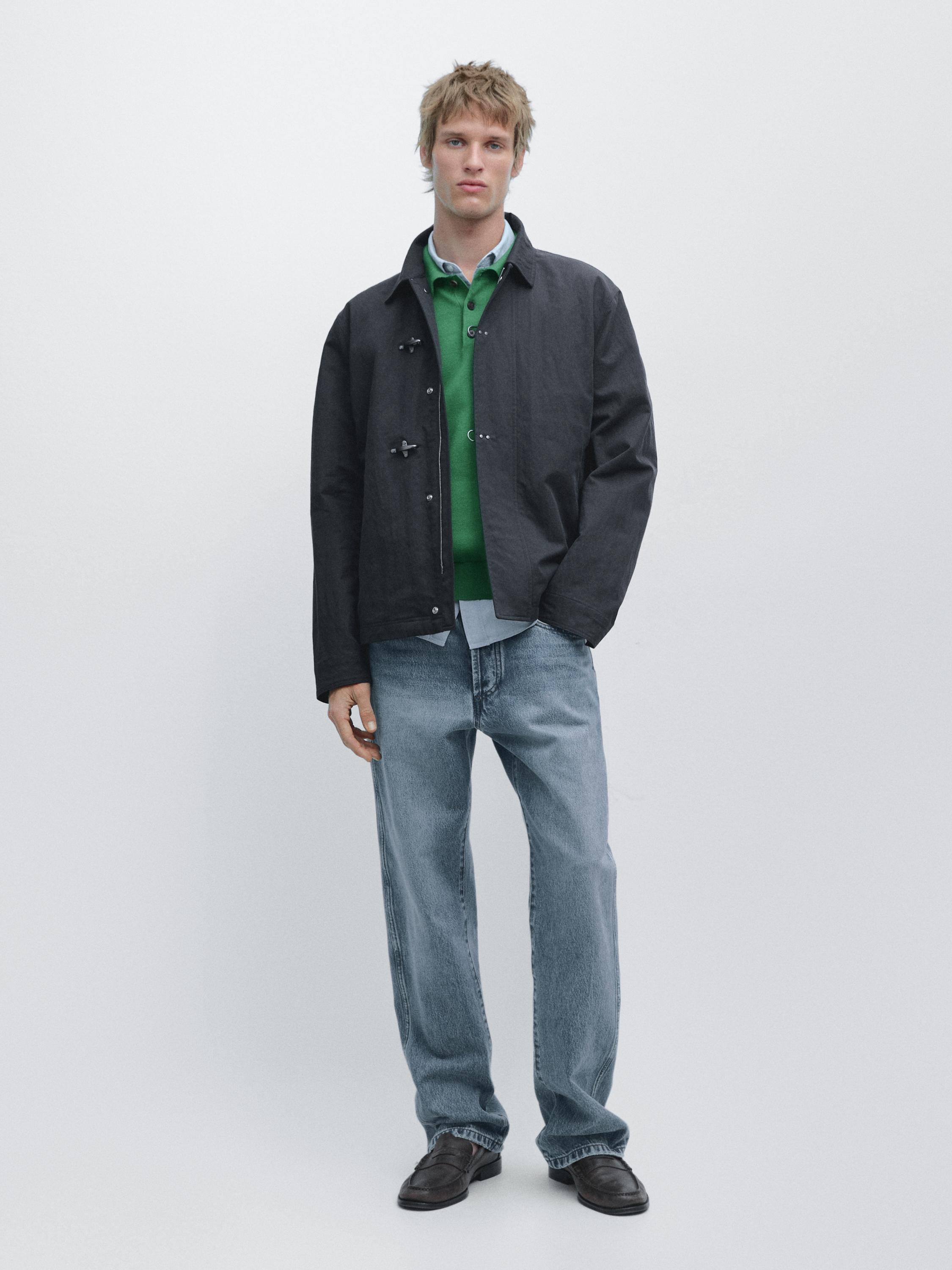 Navy blue jacket set with frogging, green sweater, light blue shirt, blue jeans, and dark shoes.