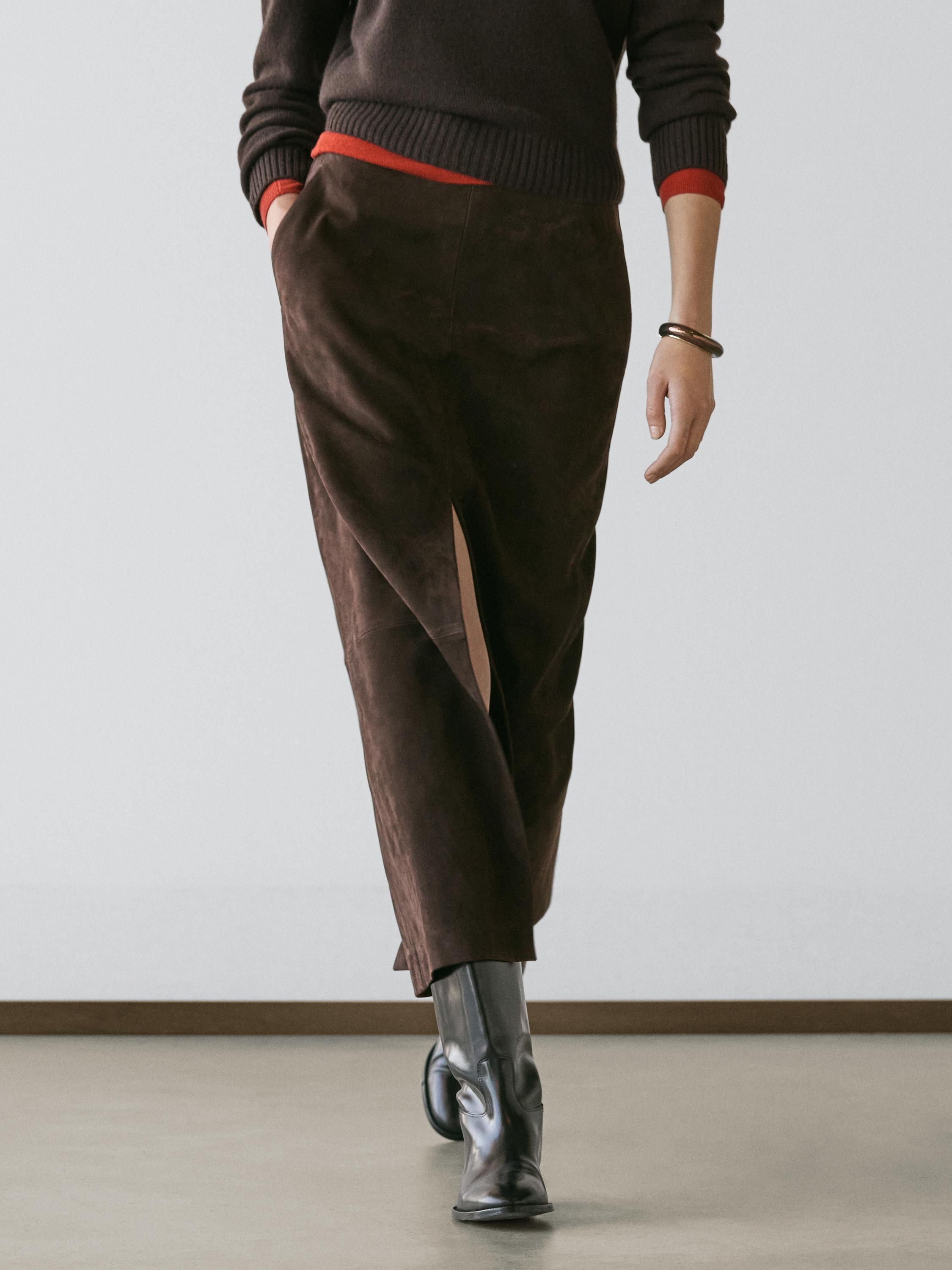 Braunes Midirock-Set mit Frontschlitz und Seitentaschen, dunklem Pullover und schwarzen Stiefeln.