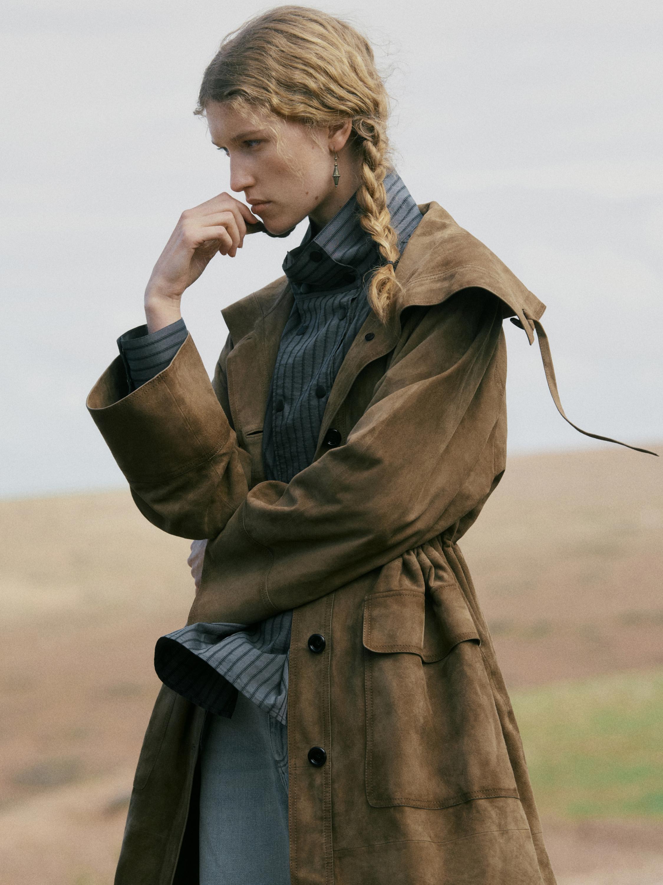 Plan moyen d'un manteau marron avec revers et poches avant à rabat, par-dessus une chemise rayée grise.