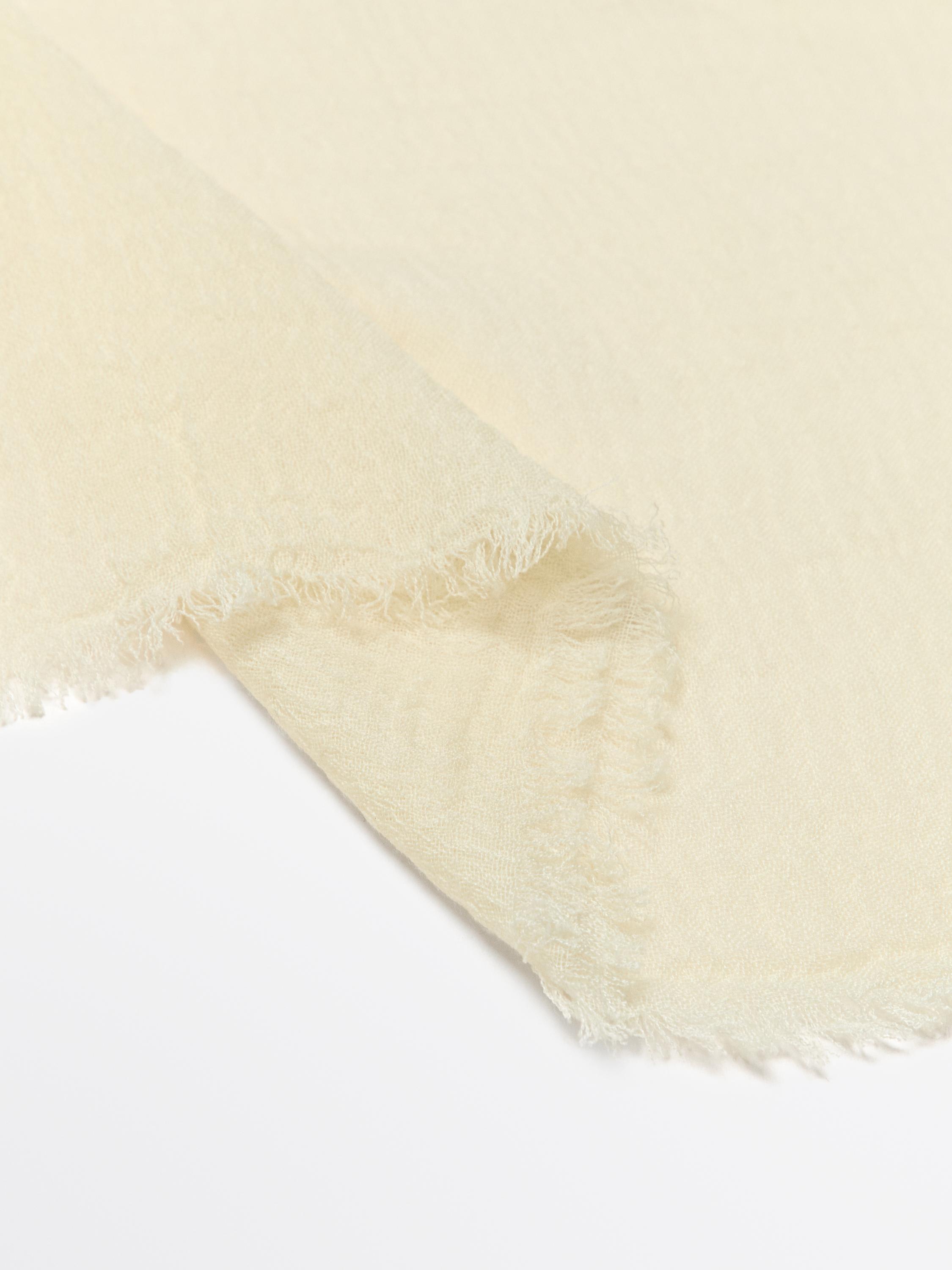 Detalle de una mascada amarilla con los bordes deshilachados.