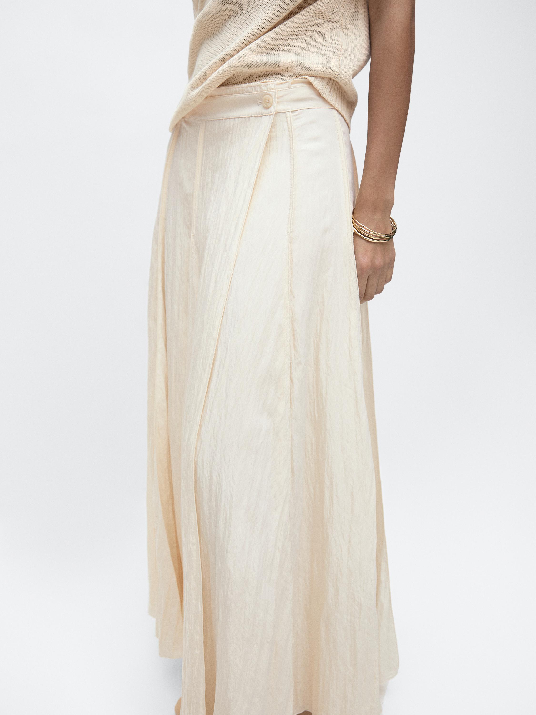Mid-shot of a beige midi skirt with a cummerbund detail and pleats, side view.