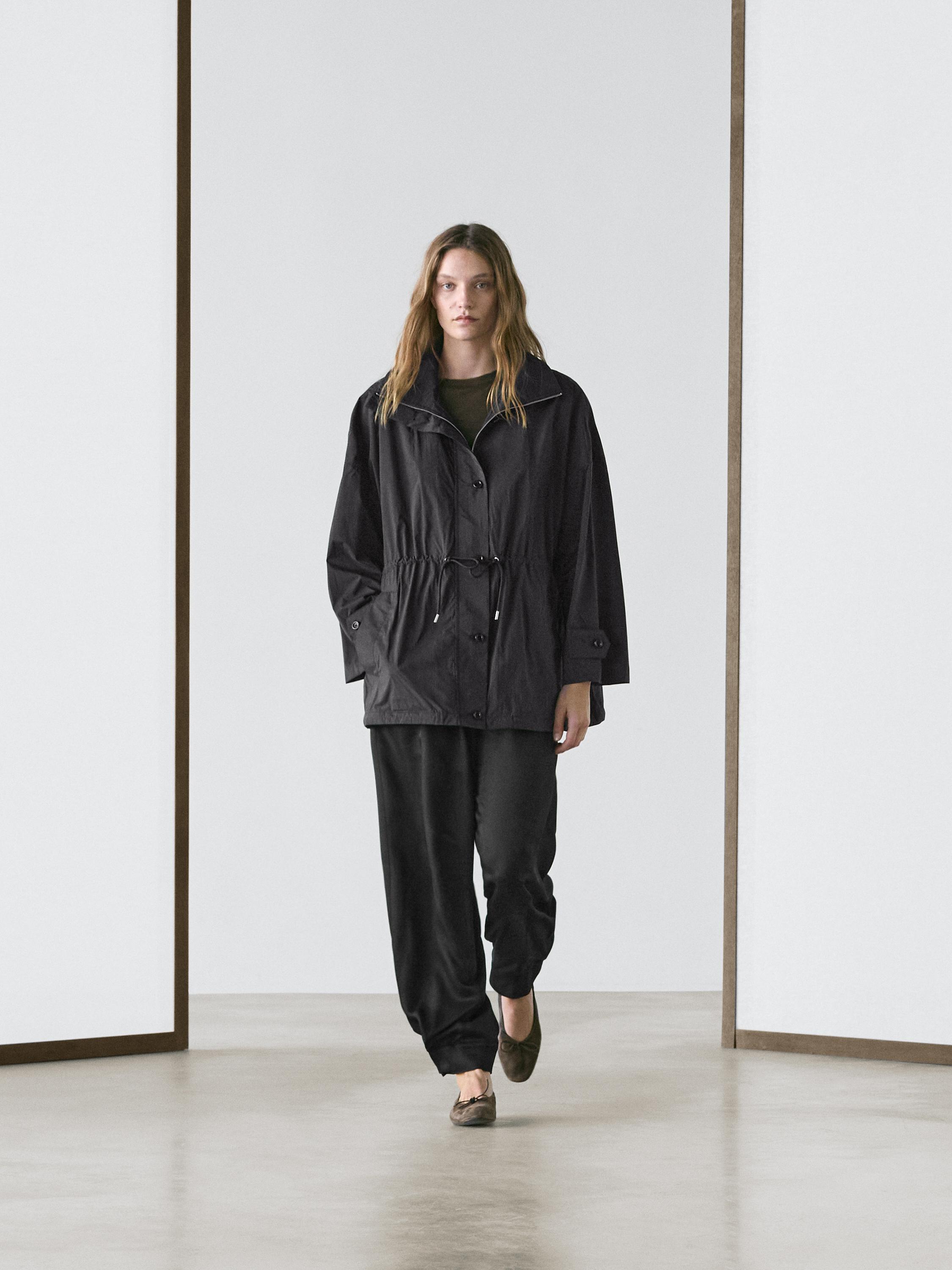 Dark blue parka set with adjustable drawstring and buttons, loose black pants, and brown flat shoes.