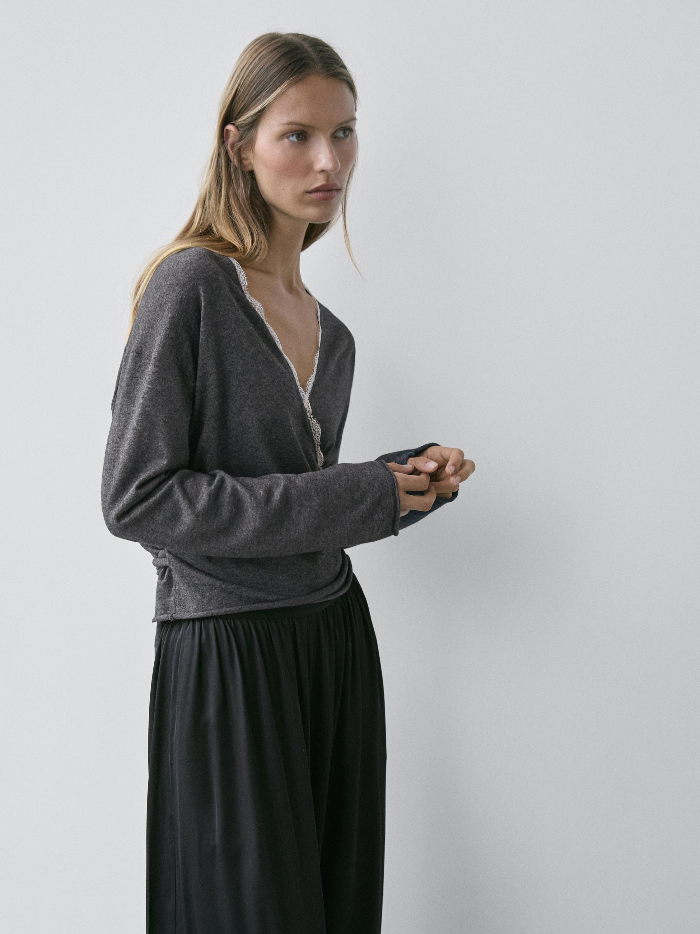 Piano medio di cardigan grigio antracite incrociato con dettaglio in pizzo sullo scollo, abbinato a gonna nera ampia.