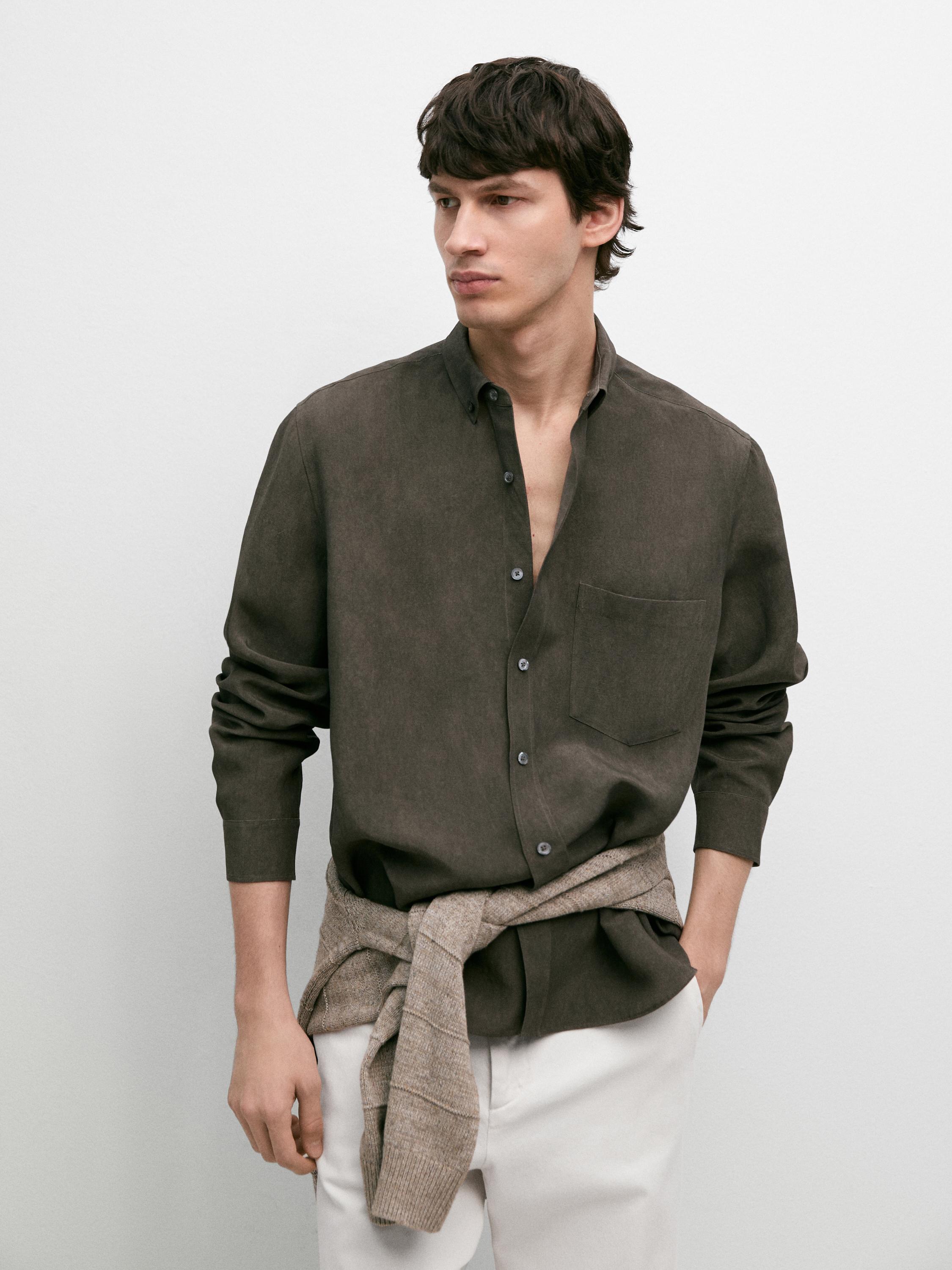 Ensemble composé d'une chemise kaki foncé à manches longues avec poche avant et boutons, d'un pantalon blanc et d'un pull beige noué à la taille.