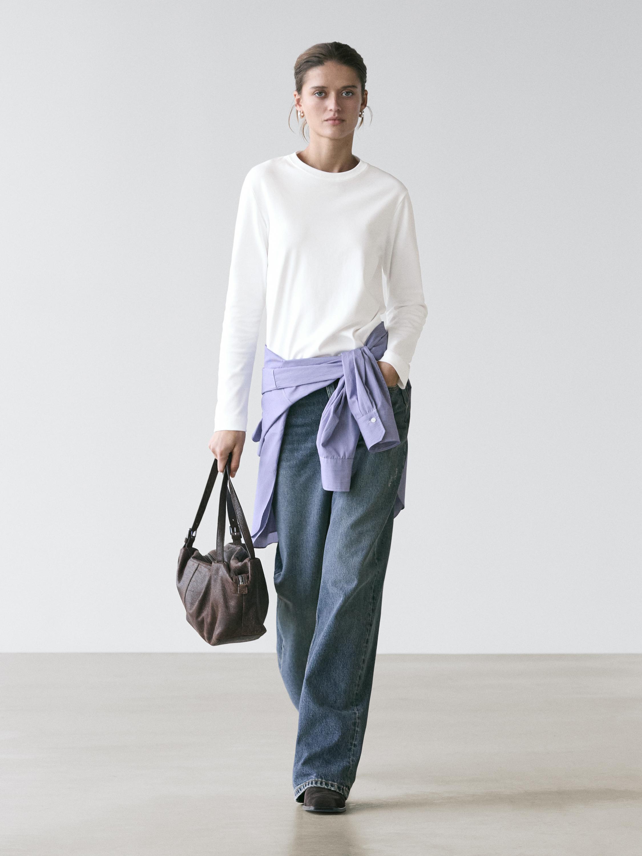 Sæt bestående af en hvid langærmet T-shirt, blå wide-leg jeans og en lilla skjorte bundet om taljen.