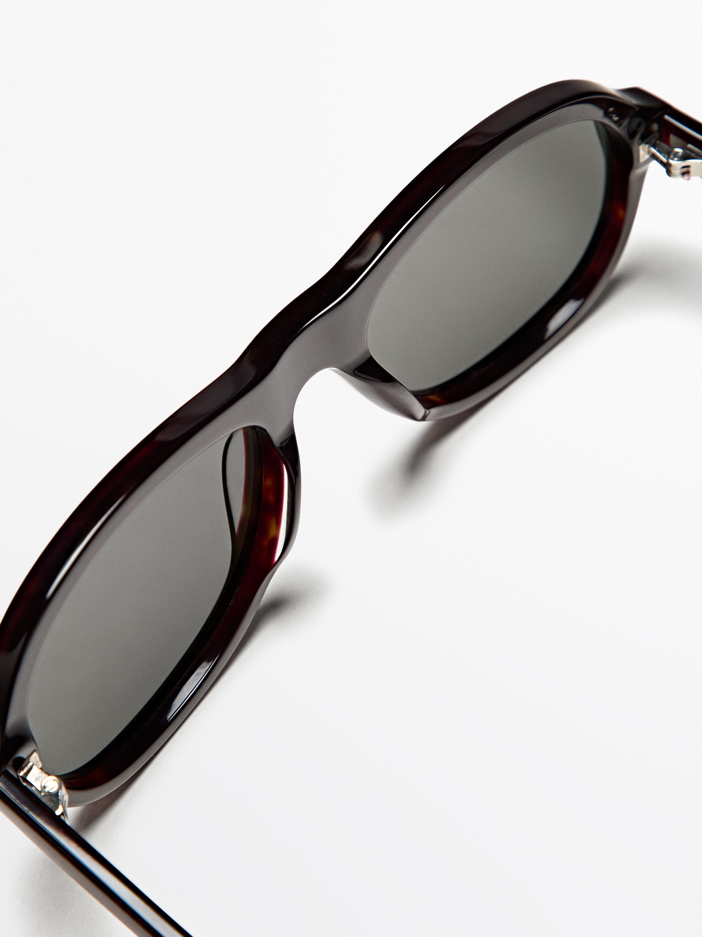 Kalın çerçeveli ve koyu renk camlı kahverengi güneş gözlüğünün detayı.