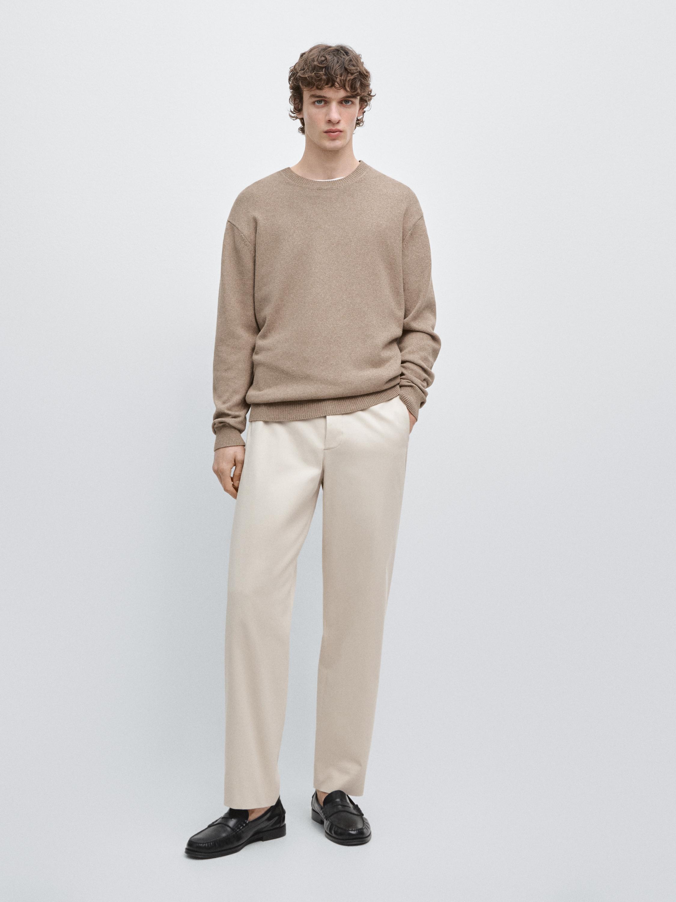 Komplet bež hlač barrel fit kroja in svetlo rjavega puloverja s črnimi čevlji.