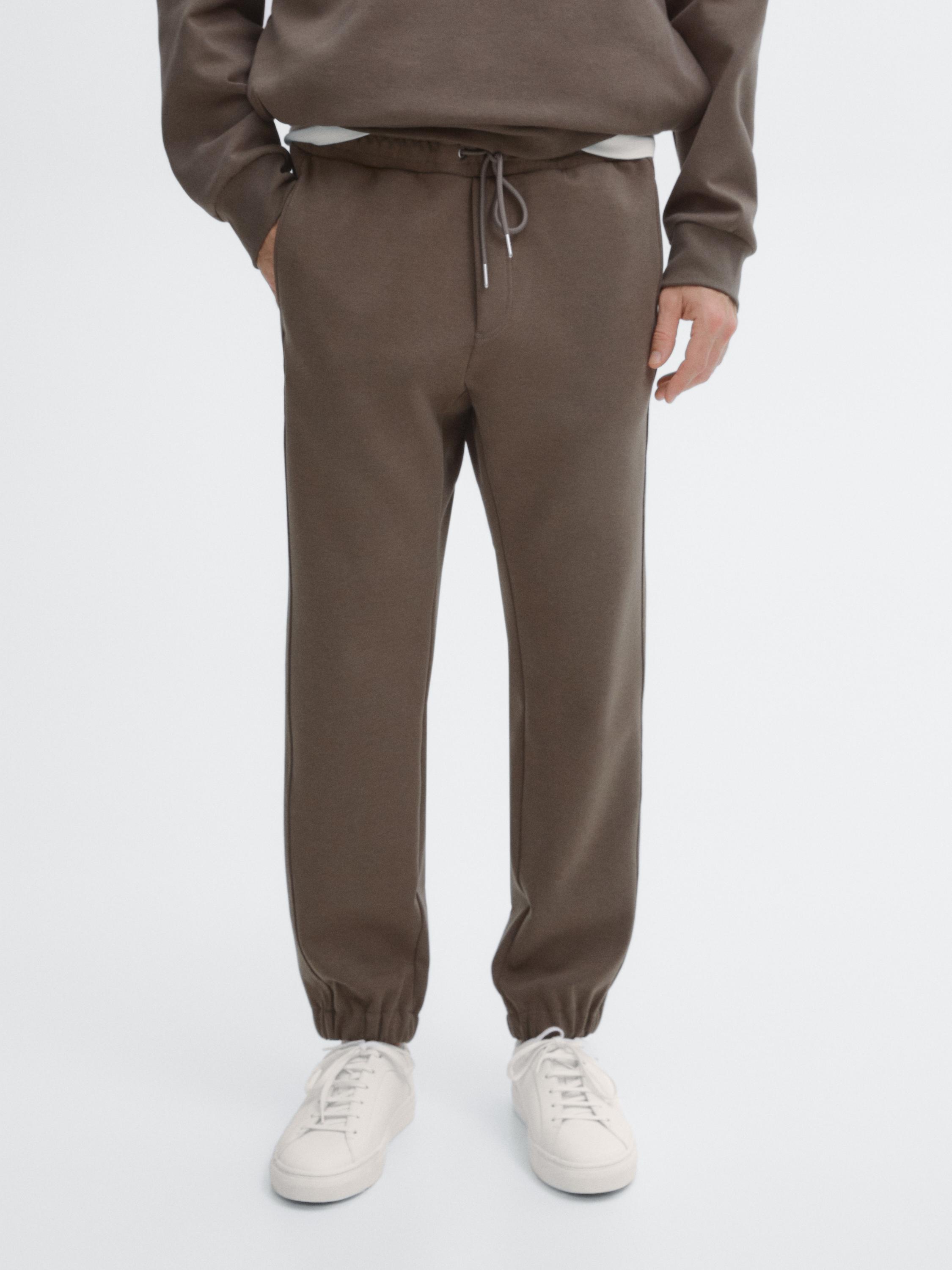 Ensemble de pantalon marron avec taille élastique et cordon de serrage ajustable, poches latérales et baskets blanches.