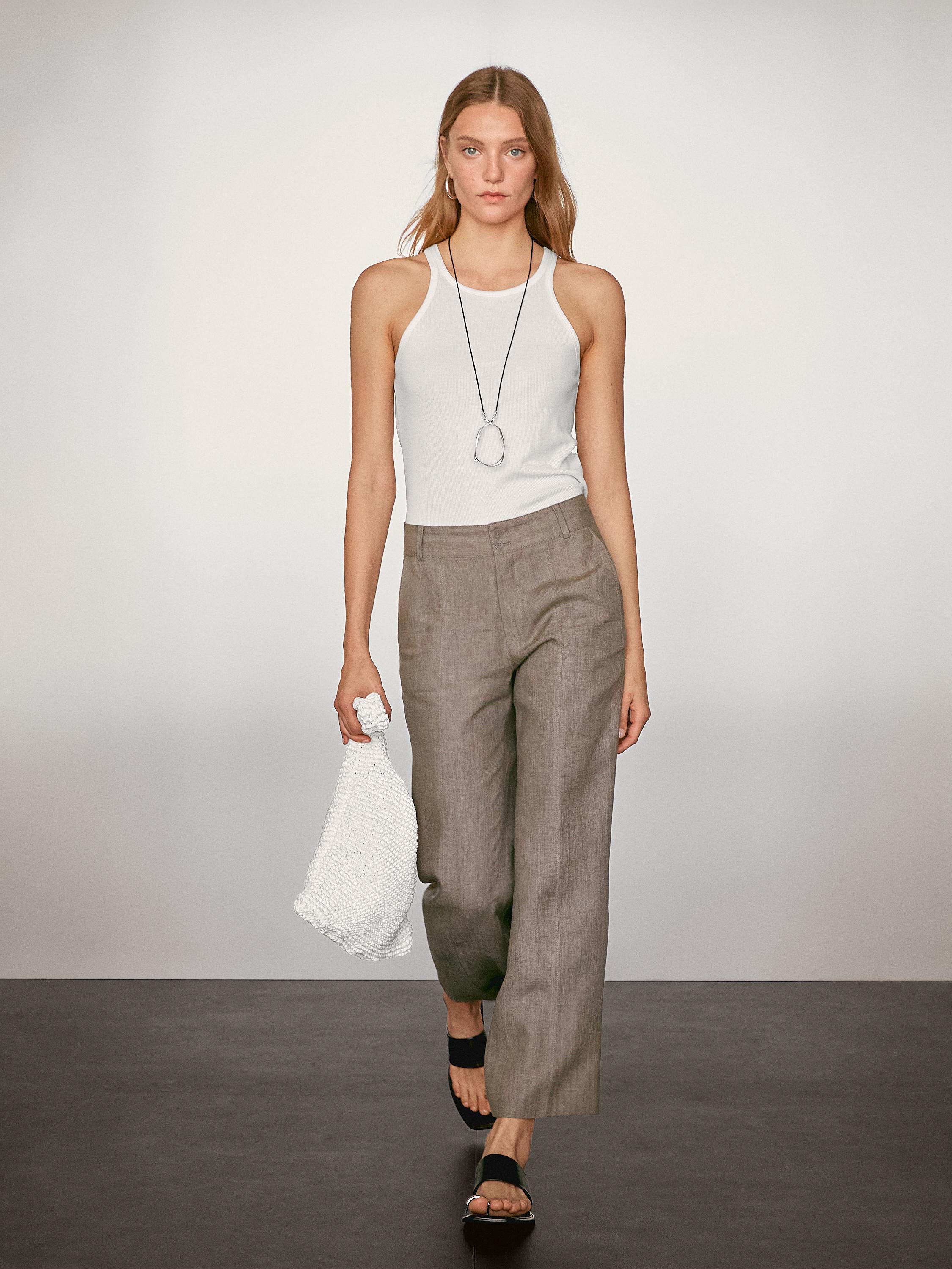 طقم مكون من تي شيرت أبيض بدون أكمام وبنطلون رمادي مع حقيبة يد بيضاء.