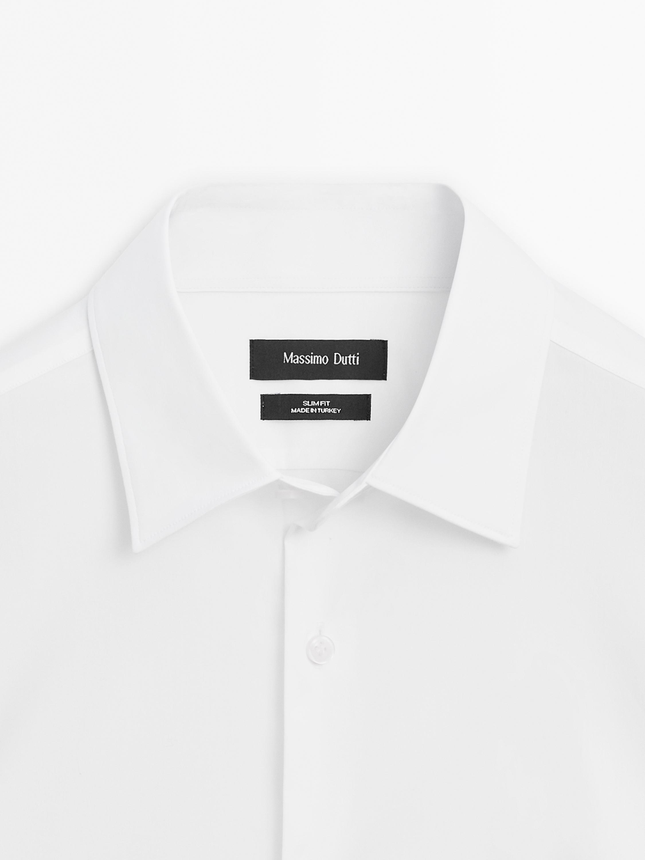 Detalhe de gola de camisa branca slim fit com carcela. Texto visível: 'Massimo Dutti', 'SLIM FIT', 'MADE IN TURKEY'.