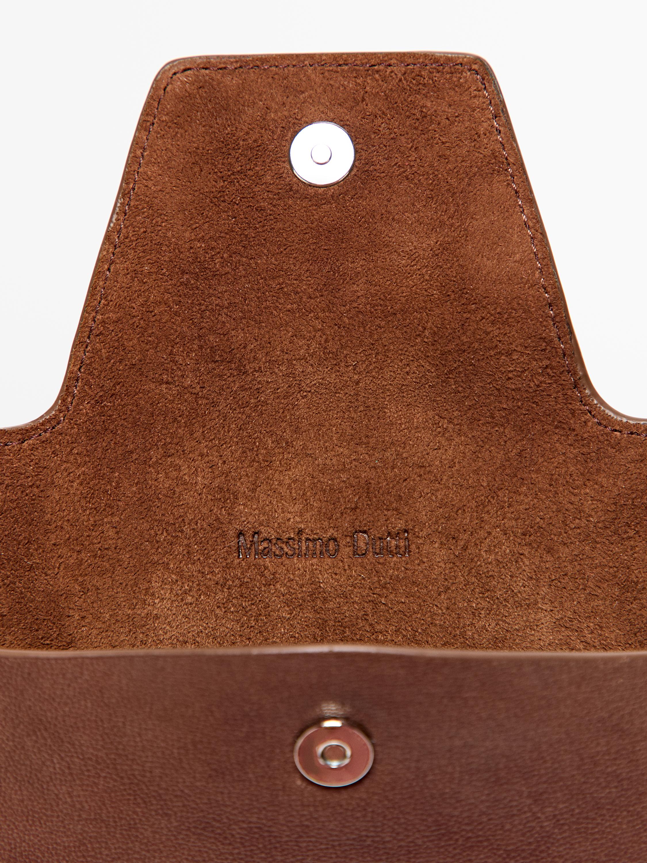 "Detail of a brown purse with a snap closure and 'Massimo Dutti' text inside."